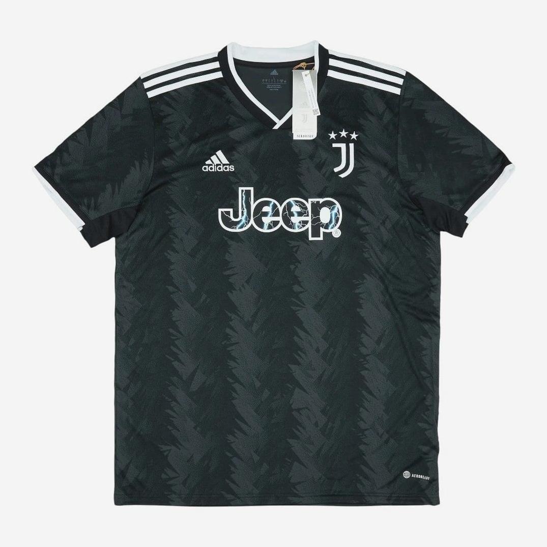 The Retro1999 Juventus 2022-23 Away Shirt is black with dark zigzag patterns, white Adidas stripes on the shoulders, and white sleeve cuffs. It features the Jeep logo, Juventus crest with three stars, and original tags on the collar.