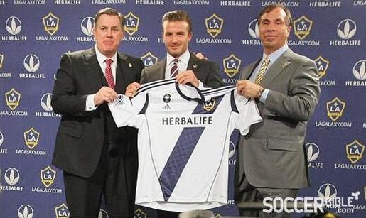 Three men in suits stand before an LA Galaxy backdrop, holding up the Retro1999 LA Galaxy 2012-13 Home Shirt with the Herbalife sponsor logo, in a moment linked to David Beckham’s final season and MLS Cup history.