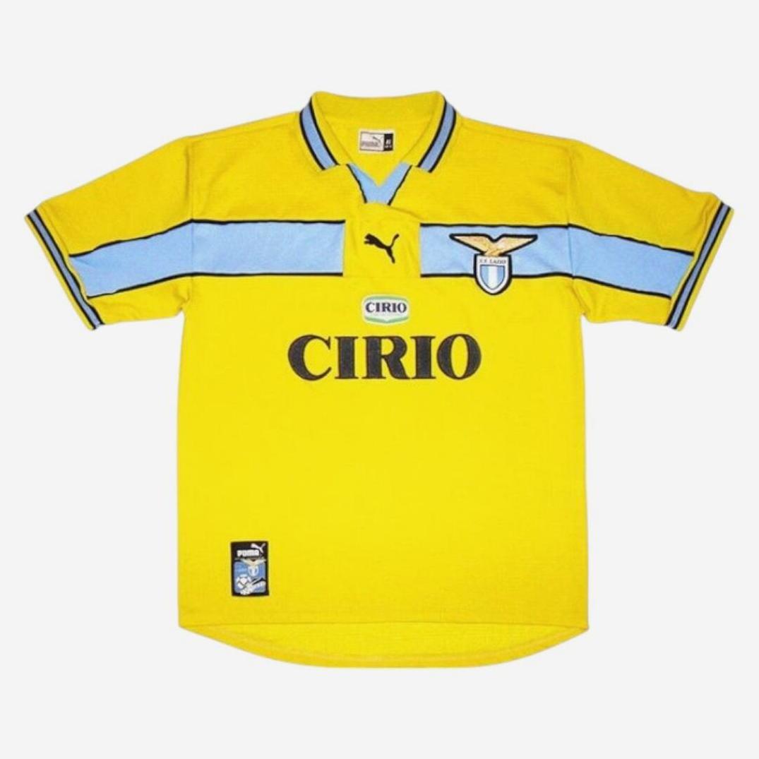The Retro1999 Lazio 1998-99 Away Shirt features yellow fabric with light blue and black accents, CIRIO sponsor text, and Lazio crest—ideal retro football memorabilia, shown flat on a white background.