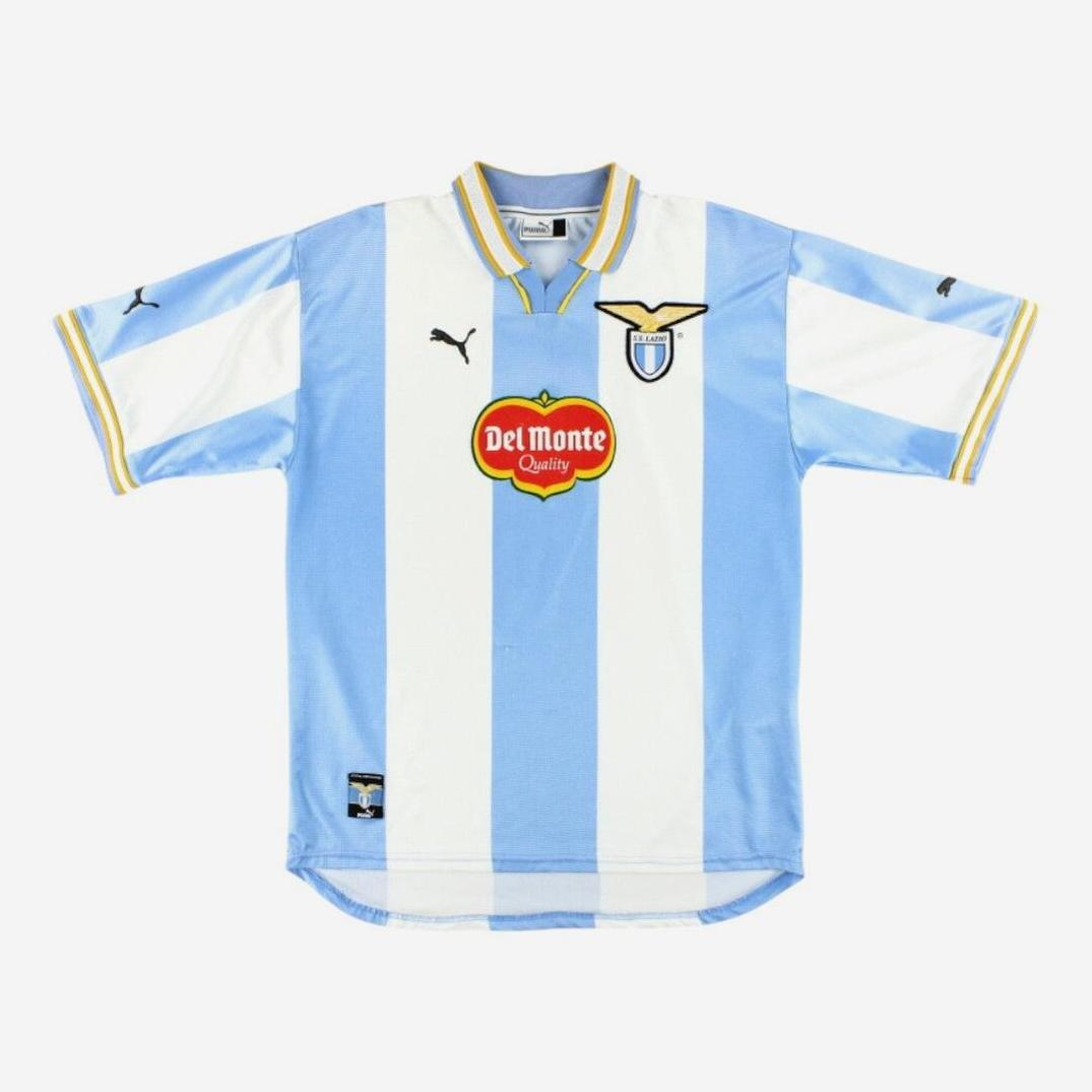 The Lazio 1999-00 Home Shirt by Retro1999 sports sky blue and white vertical stripes, black Puma logos, a red and yellow Del Monte sponsor, and the club crest—a retro classic for Serie A fans.