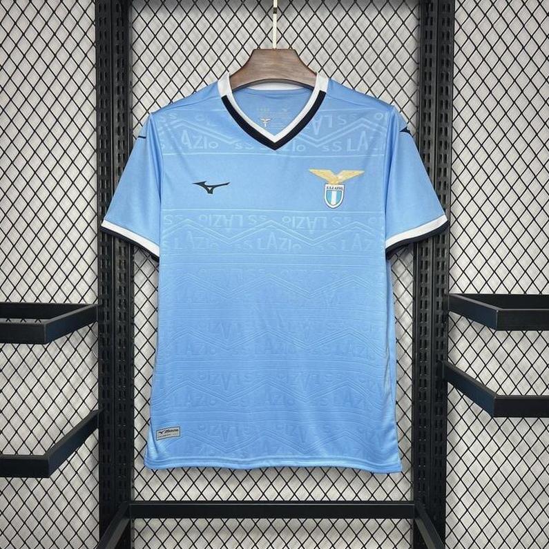 The Retro1999 Lazio 2024-25 Home Shirt in light blue with white and black trim, club crest, and Mizuno logo is displayed on a wooden hanger against a black mesh background.