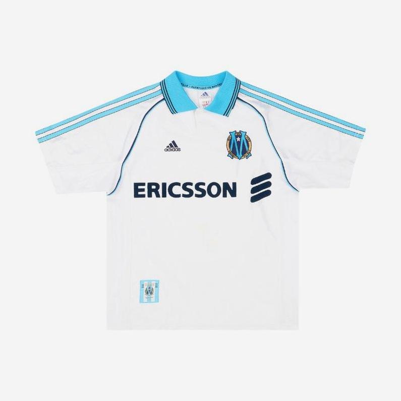 The Retro1999 Marseille 1998-99 Home Shirt is a white Ligue 1 retro kit with light blue accents, blue shoulder stripes, Ericsson sponsor logo, and OM crest badge.