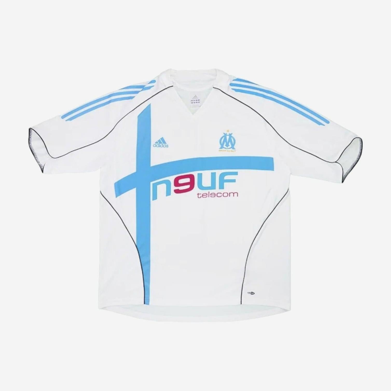The Retro1999 Marseille 2005-06 Home Shirt features blue shoulder stripes, a bold blue cross, Adidas logo, club crest, and 9UF telecom sponsor—a classic retro kit ideal for football fans.