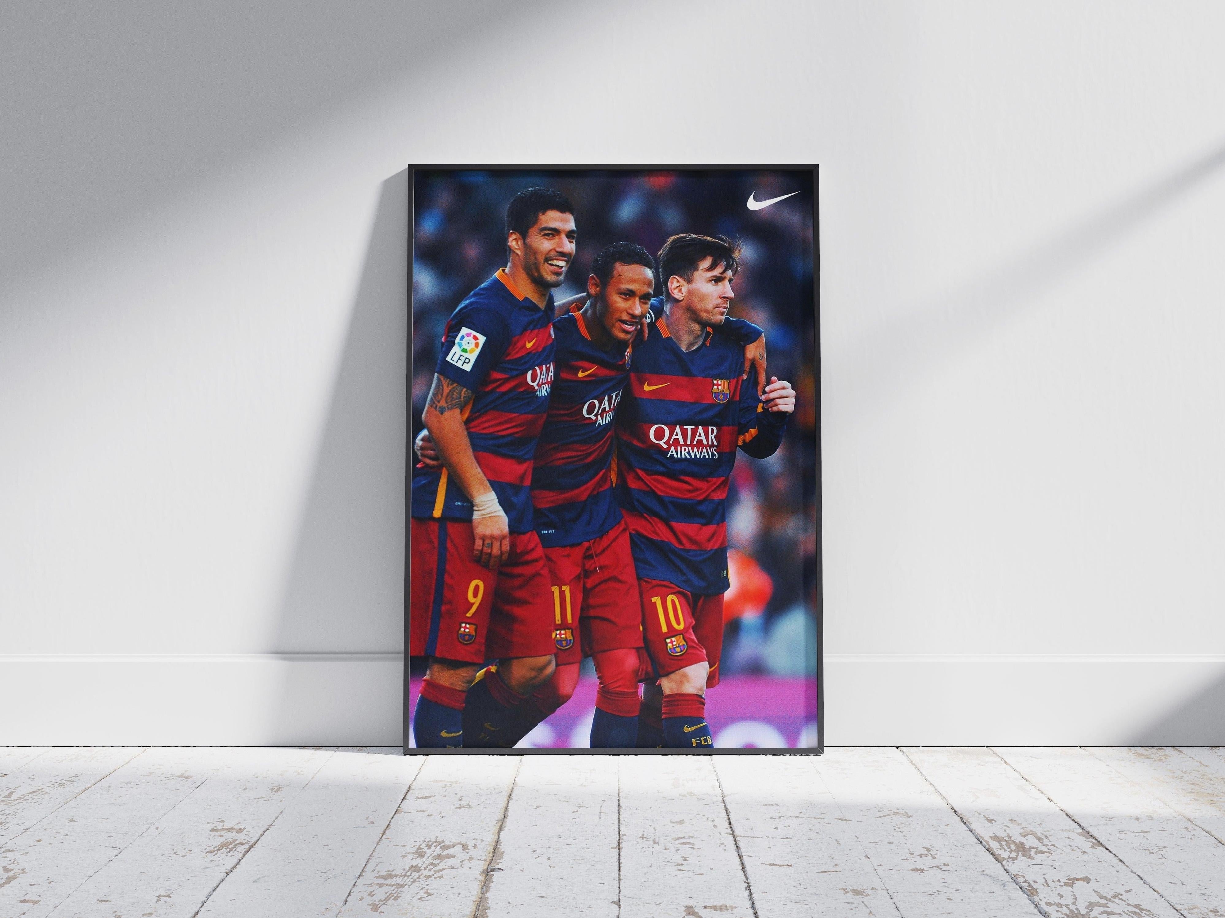 The Retro1999 Messi, Neymar, Suarez MSN Poster features the legendary Barcelona trio in blue and red kits celebrating together. Displayed upright against a white wall on a wooden floor, its a vibrant tribute to football greatness.