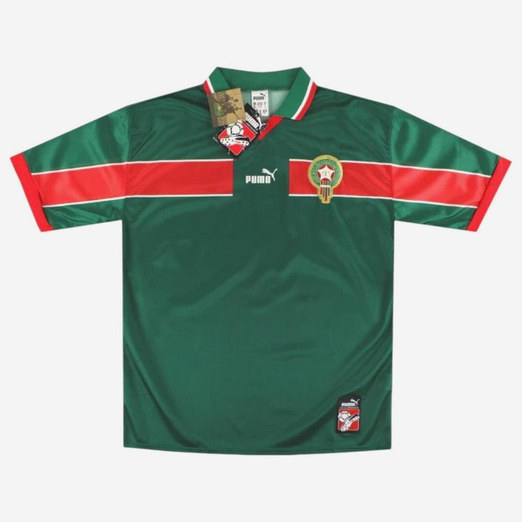The Retro1999 Morocco 1998 Home Shirt is a green short-sleeve soccer jersey with red and white stripes, featuring the Morocco national team badge and Retro1999 logo—a classic retro kit inspired by the iconic 1998 design.