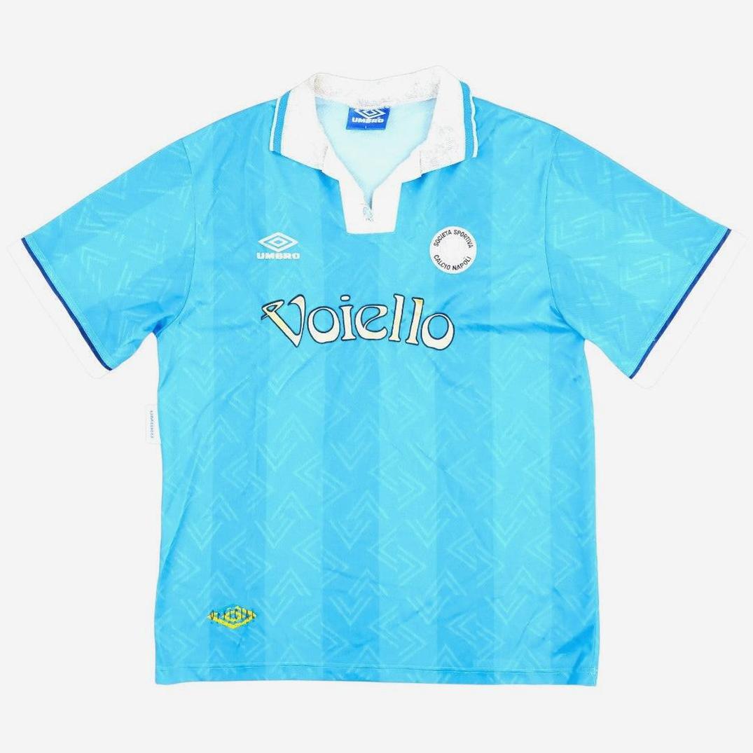 The Retro1999 Napoli 1993-94 Home Shirt features a light blue vintage design with a white collar, blue trim, and subtle patterns. This classic Serie A kit includes the Umbro logo, circular badge, and Voiello sponsor across the chest.