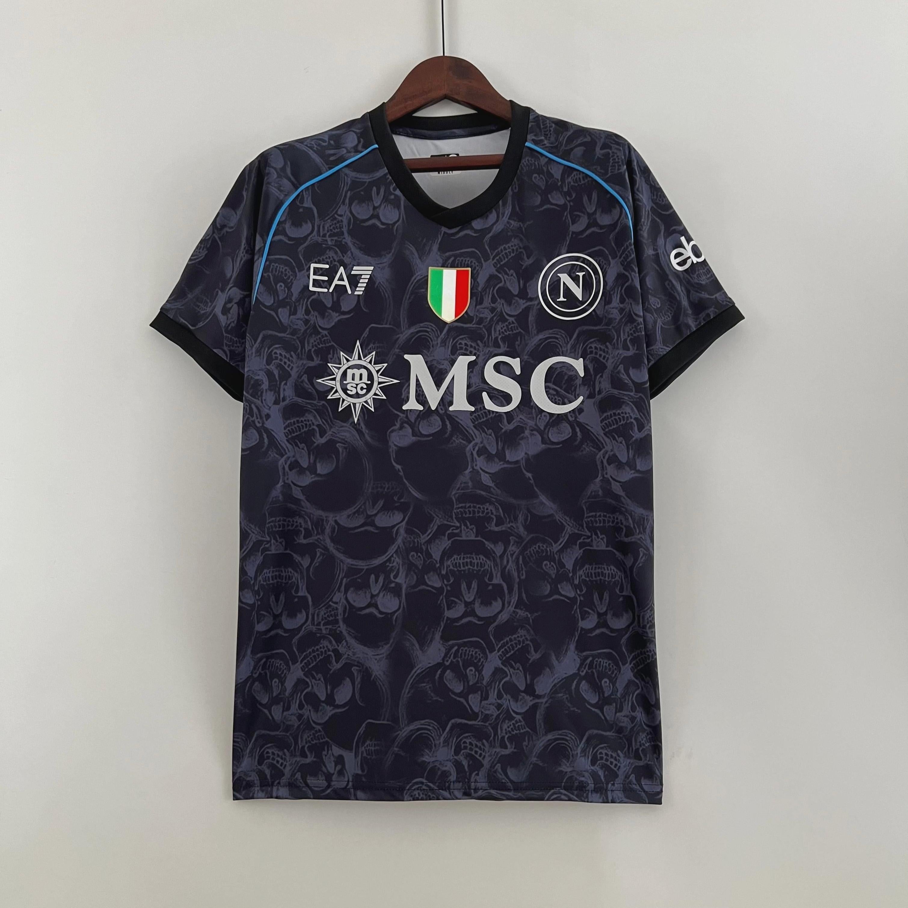The Napoli 2023-24 Halloween Edition jersey by Retro1999, featuring a subtle skull pattern, official logos, EA7 branding, MSC sponsor, Scudetto badge, and Napoli crest, hangs on a wooden hanger against a white background.
