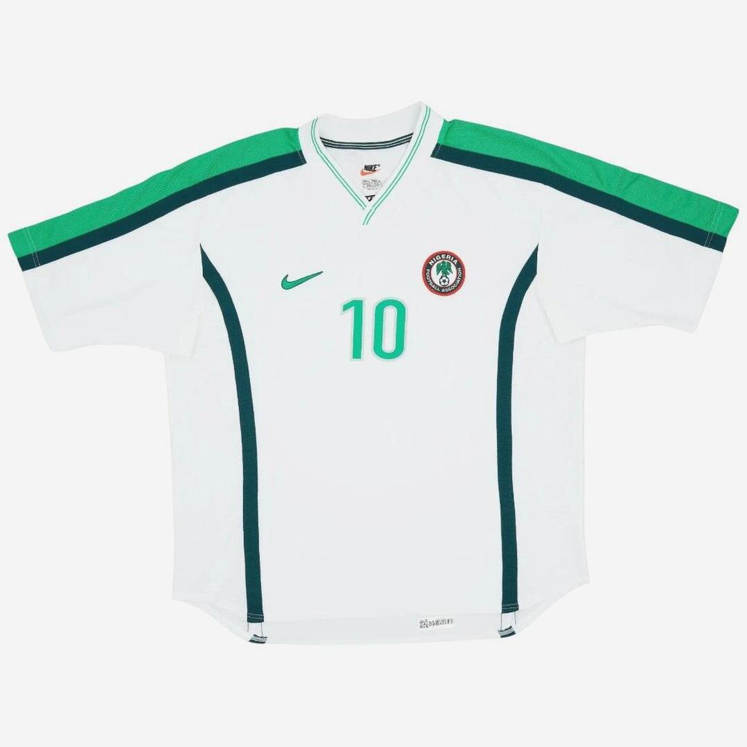 The Nigeria 1998 Away Shirt by Retro1999 features white fabric with green shoulder stripes, dark green side accents, number 10 in green, a Nike logo, and the Nigerian Football Federation crest—a retro nod to Nigerian football history.