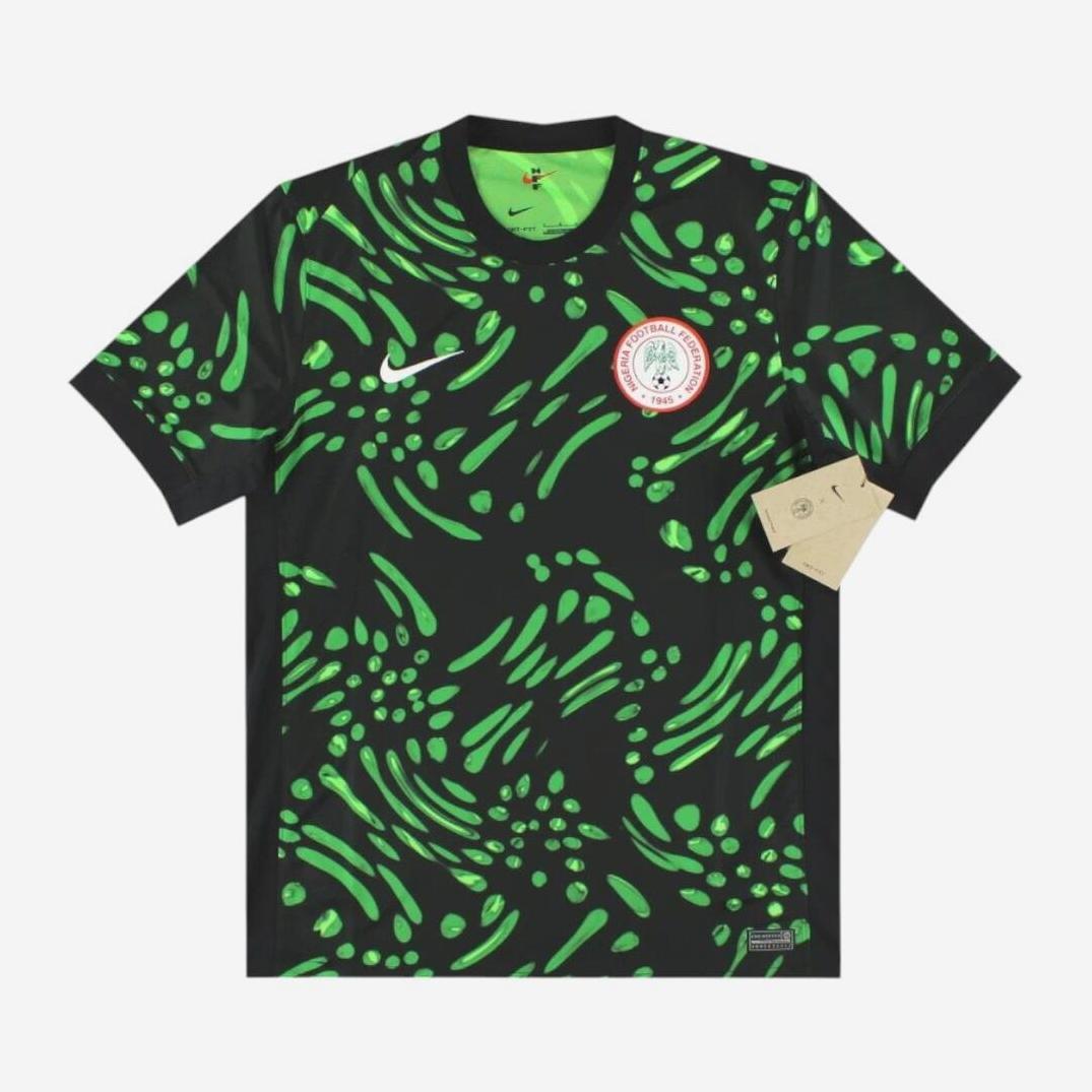 The Retro1999 Nigeria 2024 Away Shirt features black short sleeves, bright green abstract patterns, a white Nike logo, a Nigeria Football Federation badge on the chest, and an authentic design with premium materials and a brown tag.