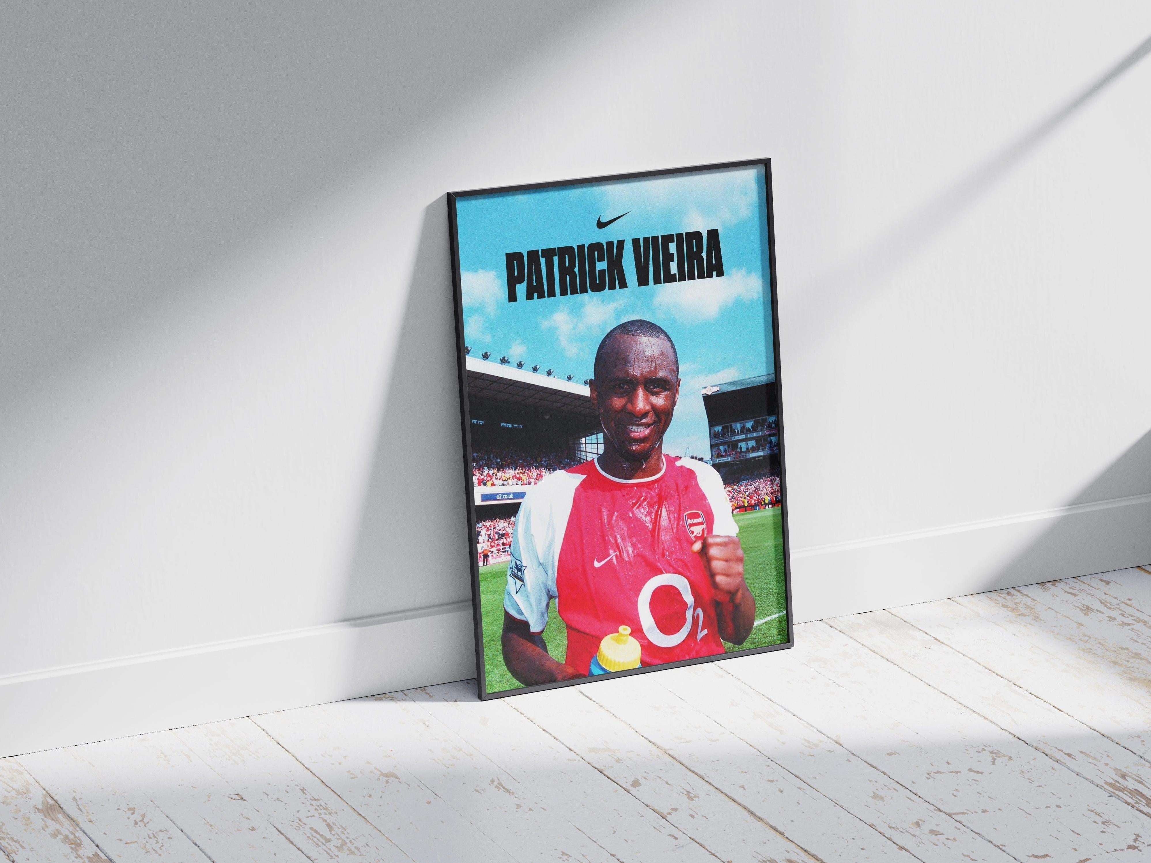 The Retro1999 Patrick Vieira x Arsenal Poster shows the football legend smiling in his Arsenal jersey, holding a yellow bottle, with a stadium backdrop and bold PATRICK VIEIRA text for a standout look on any wall.