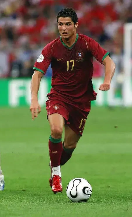 A soccer player wearing the Retro1999 Portugal 2006 Home Shirt (number 17) runs on a green field, controlling a black and white ball, with a blurred crowd in the background—highlighting classic national football shirt style.