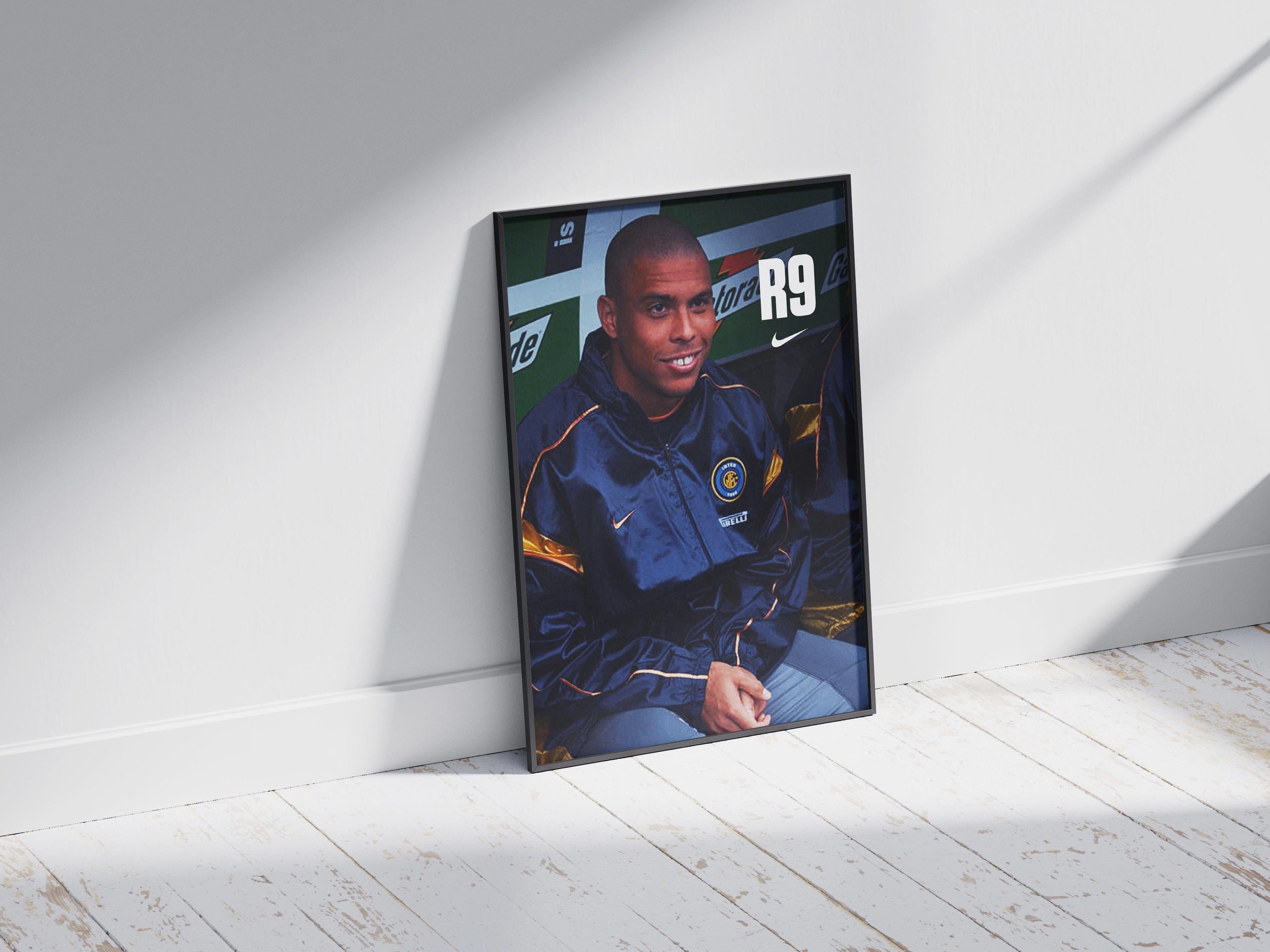 The R9 x Inter Poster by Retro1999 features a soccer player in a navy Inter Milan jacket, sitting and smiling. Propped against a white wall on a wooden floor, sunlight and shadows add an elegant football vibe.