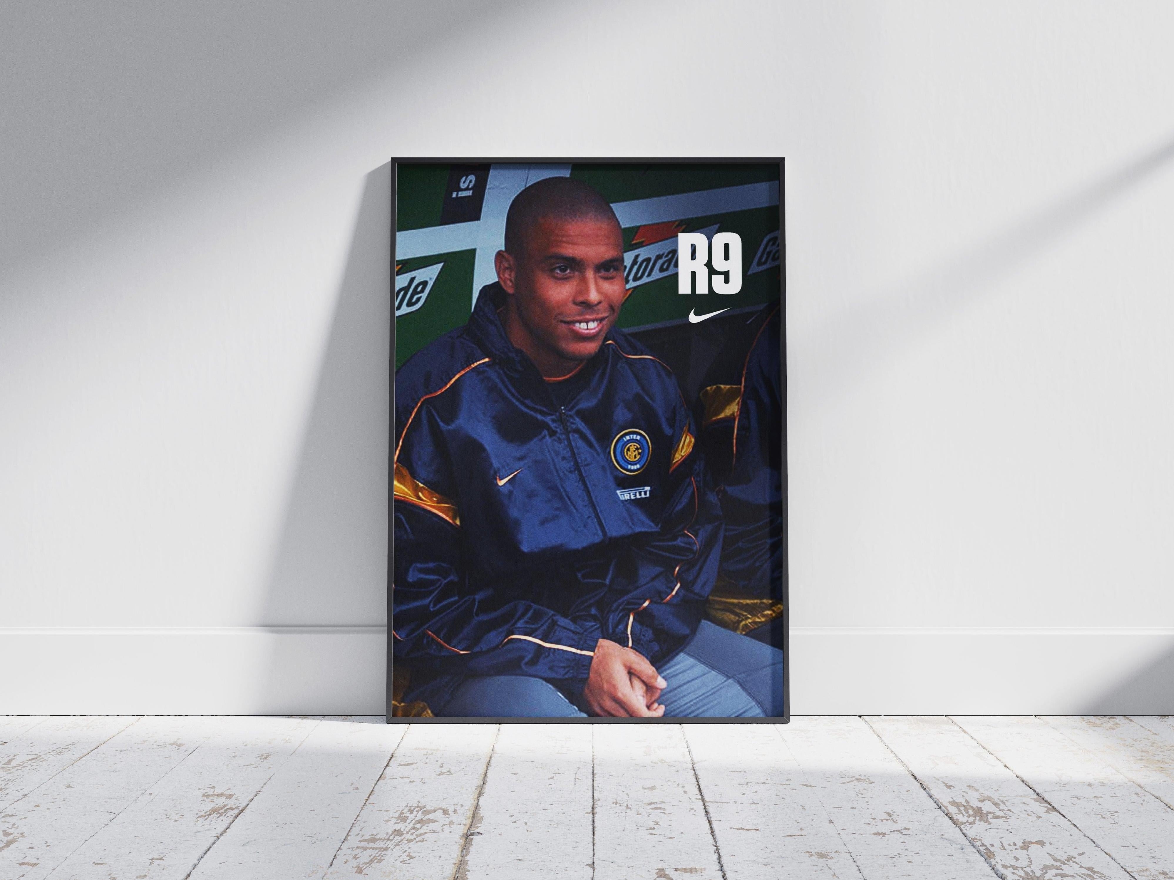 The Retro1999 R9 x Inter Poster features a smiling player in an Inter Milan jacket sitting on a bench, with R9 on the top right, framed and propped against a white wall on a wooden floor.