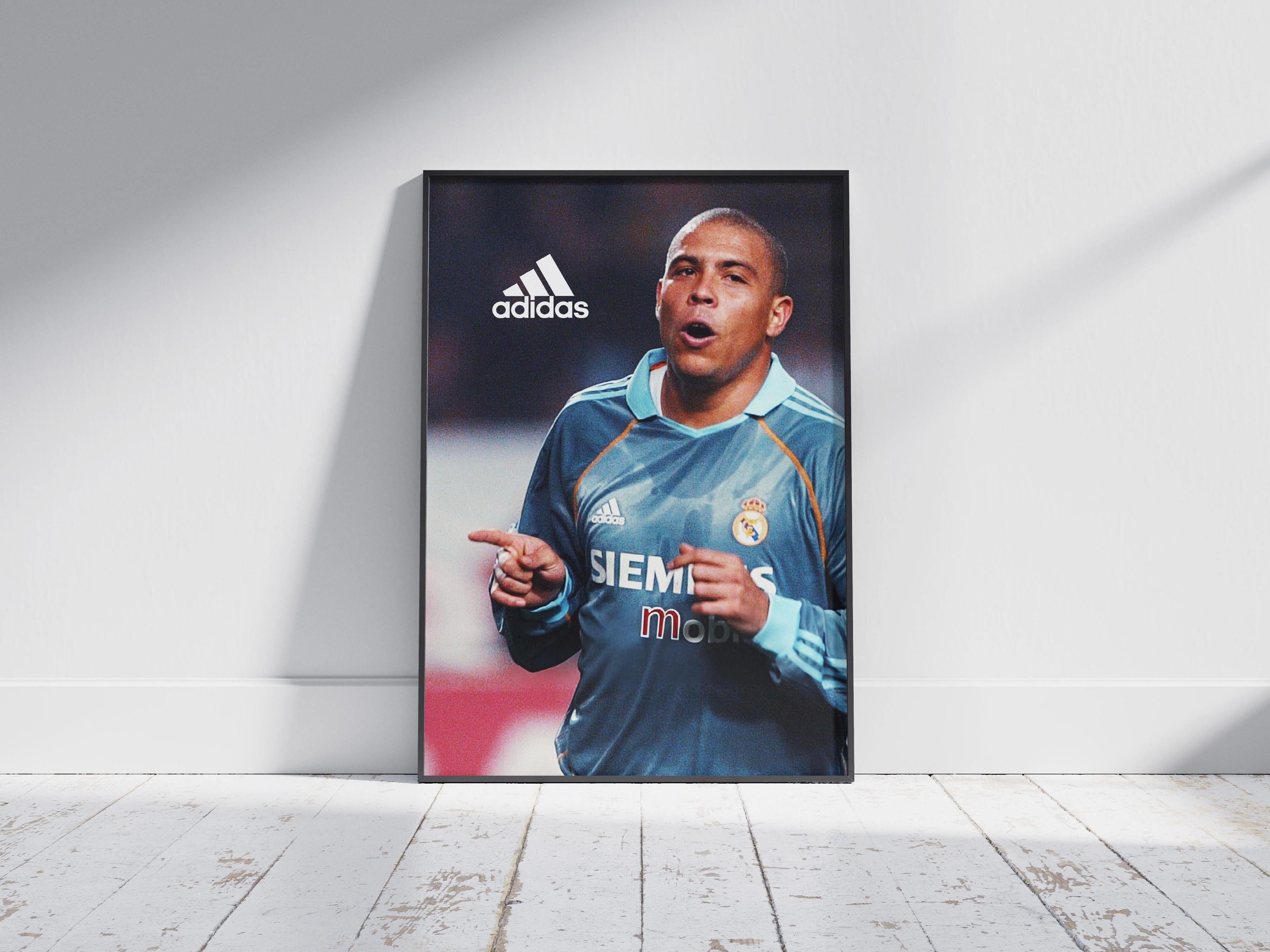 The R9 x Real Madrid Poster by Retro1999 shows a footballer in a blue jersey pointing with both hands, on a wooden floor. Visible are the Adidas logo and “Siemens mobile” sponsor, capturing the essence of the Spanish Primera Liga.
