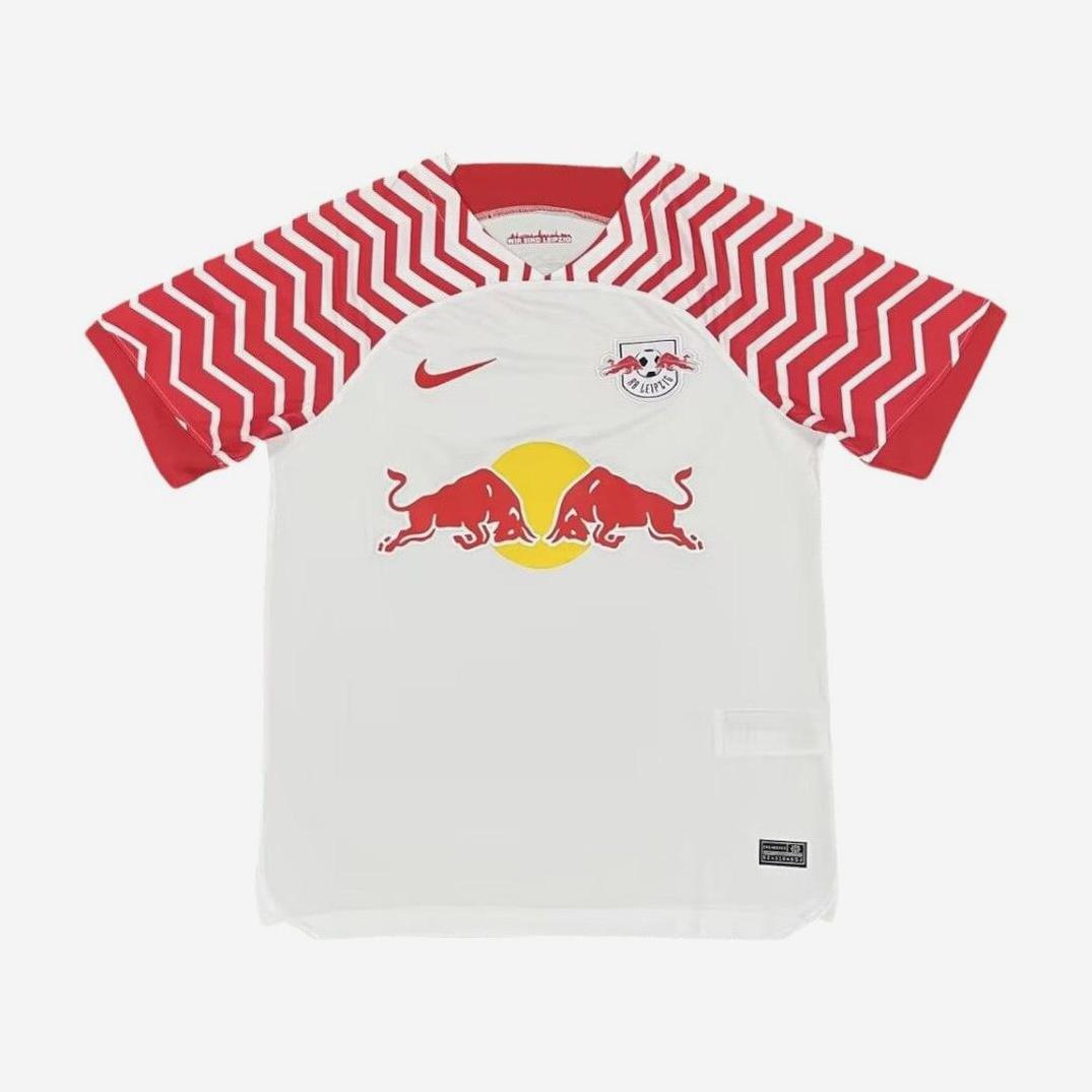 The Retro1999 RB Leipzig 2023-24 Home Shirt is white with red zigzag sleeves, a chest club crest, red Nike logo, and bold Red Bull branding—a stylish retro kit for Bundesliga fans.