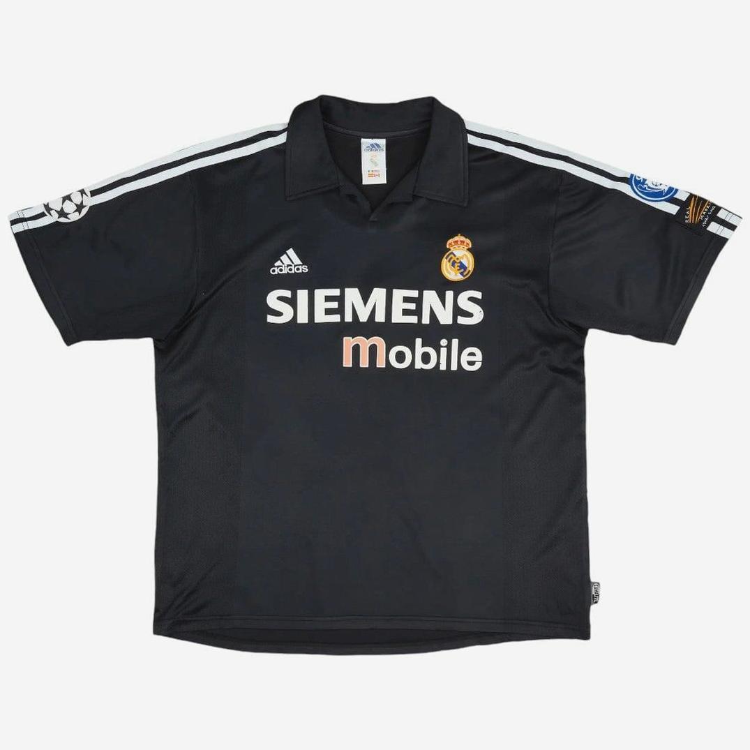 The Retro1999 Real Madrid 2002-03 Away Shirt features a black design with white shoulder stripes, Siemens Mobile sponsor, Adidas logo, club crest, and UEFA Champions League patch—an iconic piece of football memorabilia.