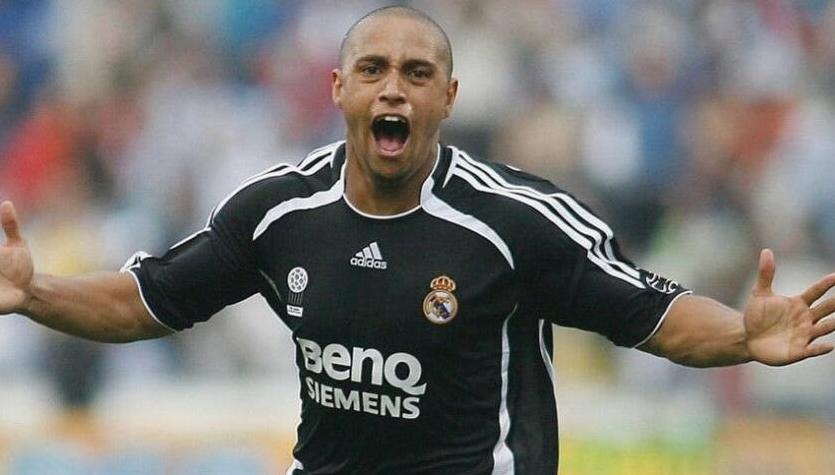 A soccer player in a Retro1999 Real Madrid 2006-07 Away Shirt celebrates with arms outstretched during a match, exuding joy and energy—perhaps after a key win en route to a La Liga title.