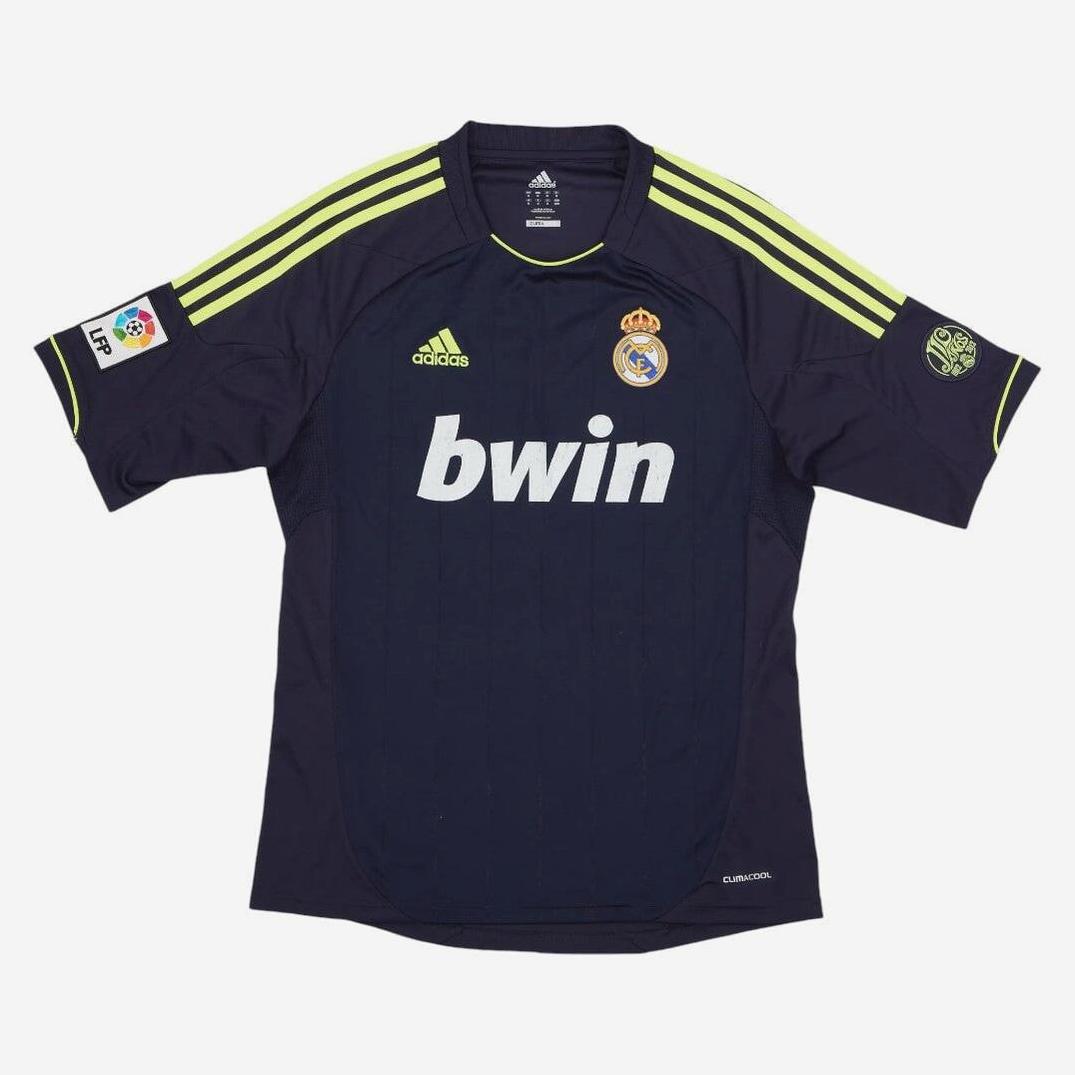 The Retro1999 Real Madrid 2012-13 Away Shirt features navy blue fabric, yellow-green shoulder stripes, bwin front sponsor, club crest on the chest, plus La Liga and sponsor sleeve patches—a must-have retro kit for fans.