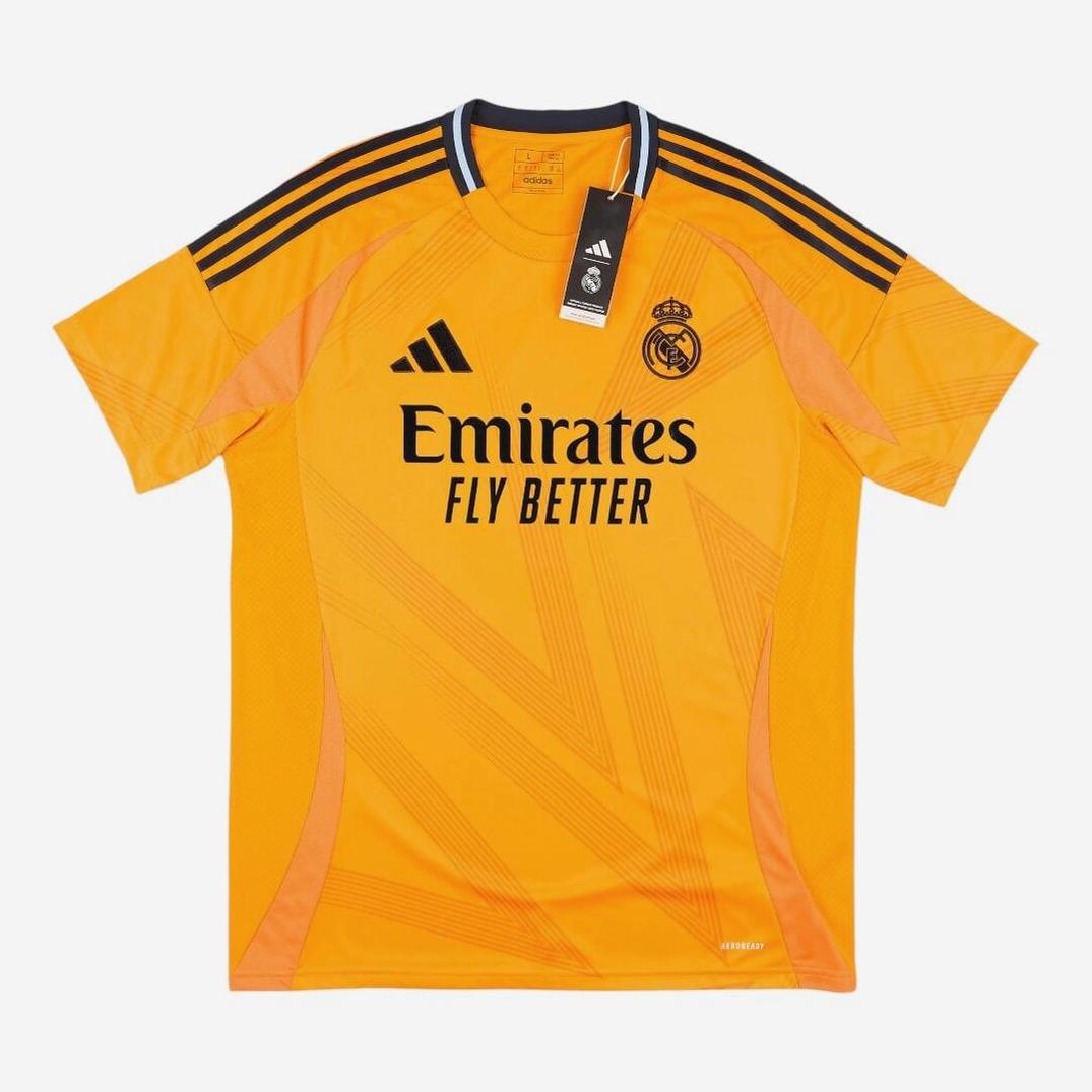 The Real Madrid 2024-25 Away Shirt by Retro1999 features an orange design with black Adidas stripes, club crest, and Emirates Fly Better logo. This La Liga retro kit is new with tags and displayed flat on a white background.