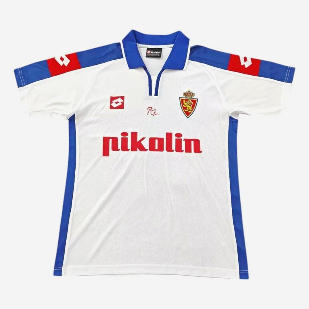 The Real Zaragoza 2003-05 Home Shirt by Retro1999 is a white and blue top with red details, club crest, red pikolín sponsor, and Lotto shoulder logos—a classic La Liga kit popular among vintage football shirt collectors.