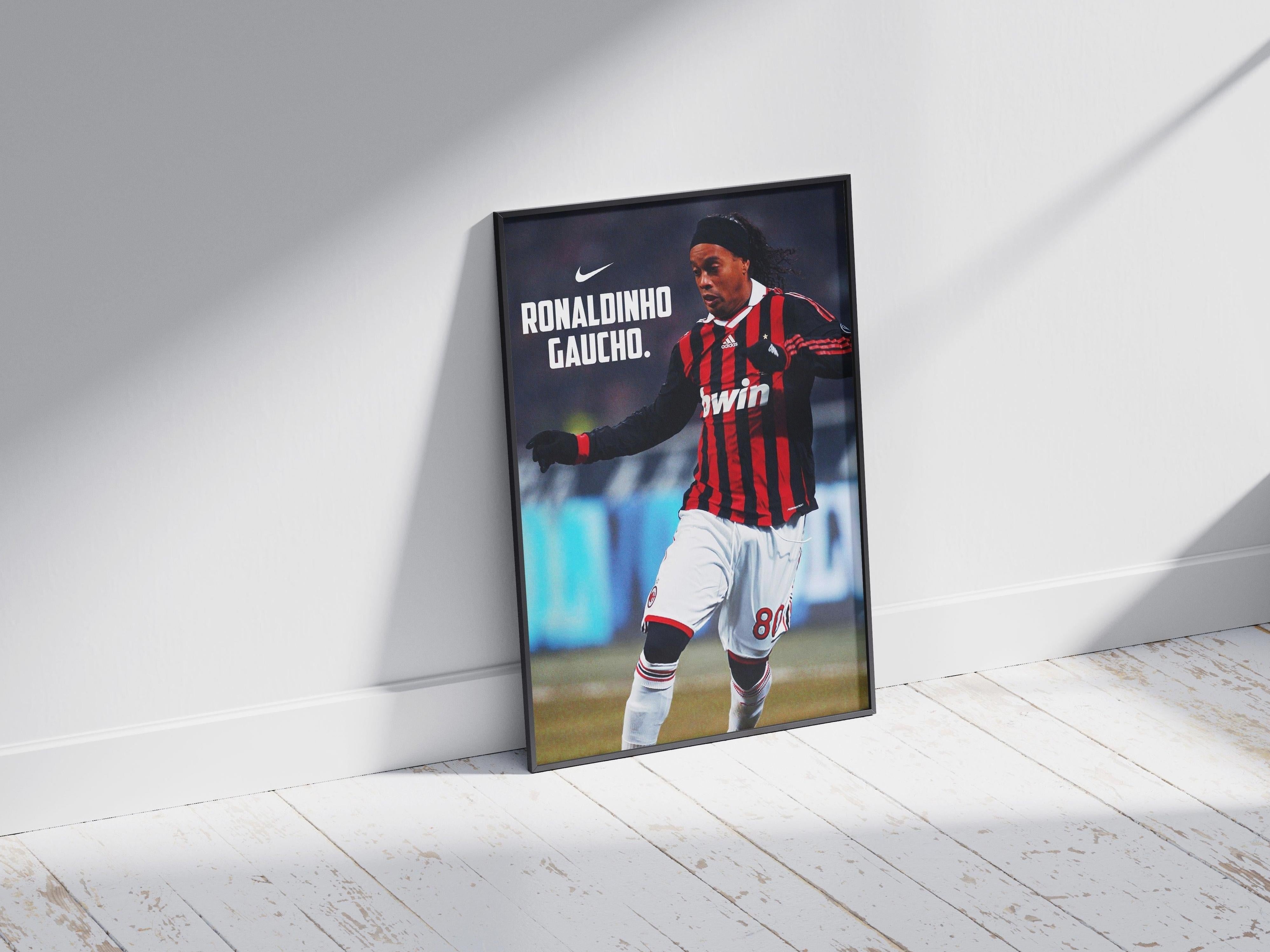The Retro1999 Ronaldinho Gaucho x AC Milan Poster, featuring him in a #11 kit, is framed and set on a wooden floor against a white wall—a standout sports collectible brightened by sunlight.