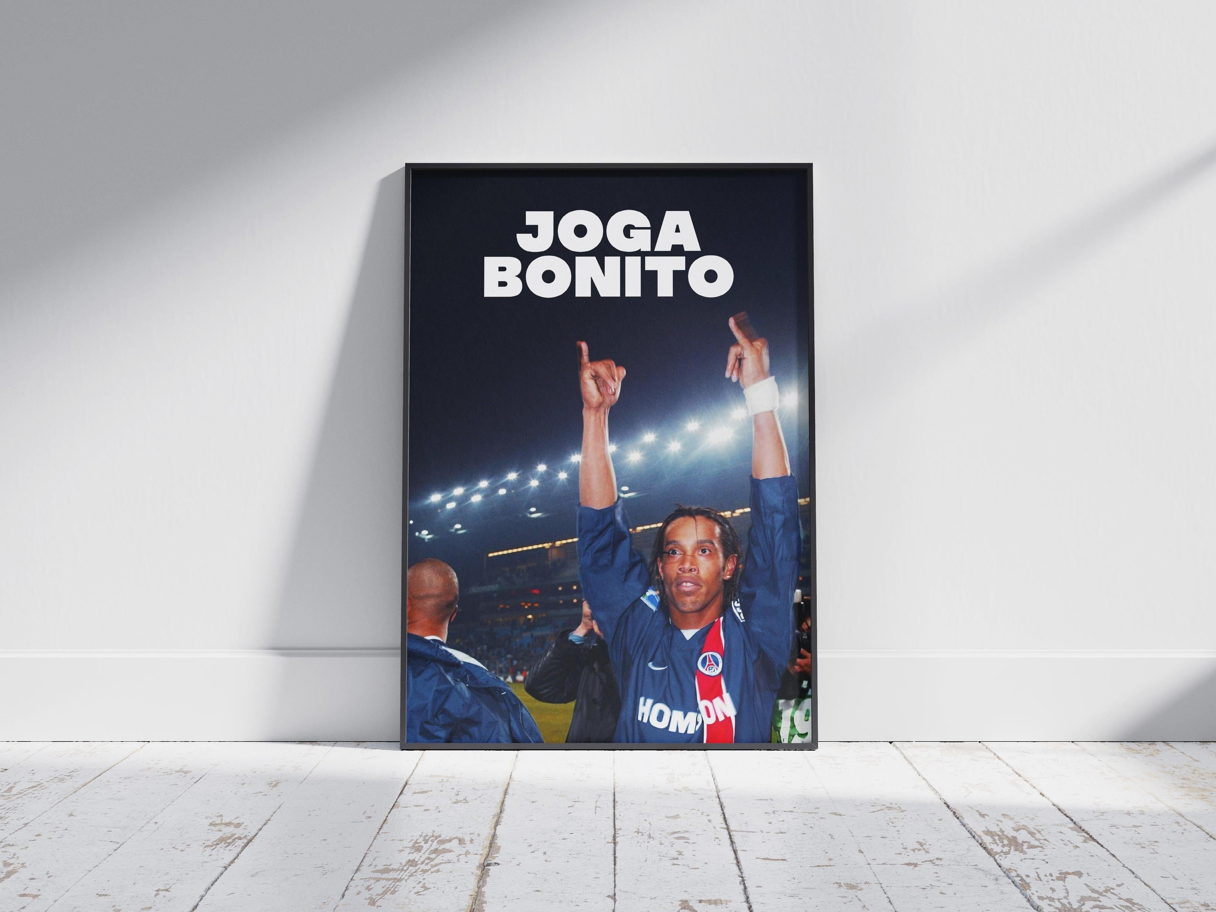 The Retro1999 Ronaldinho Joga Bonito Poster features the soccer legend celebrating in a blue Paris Saint-Germain jersey, framed and leaning against a white wall on a wooden floor.