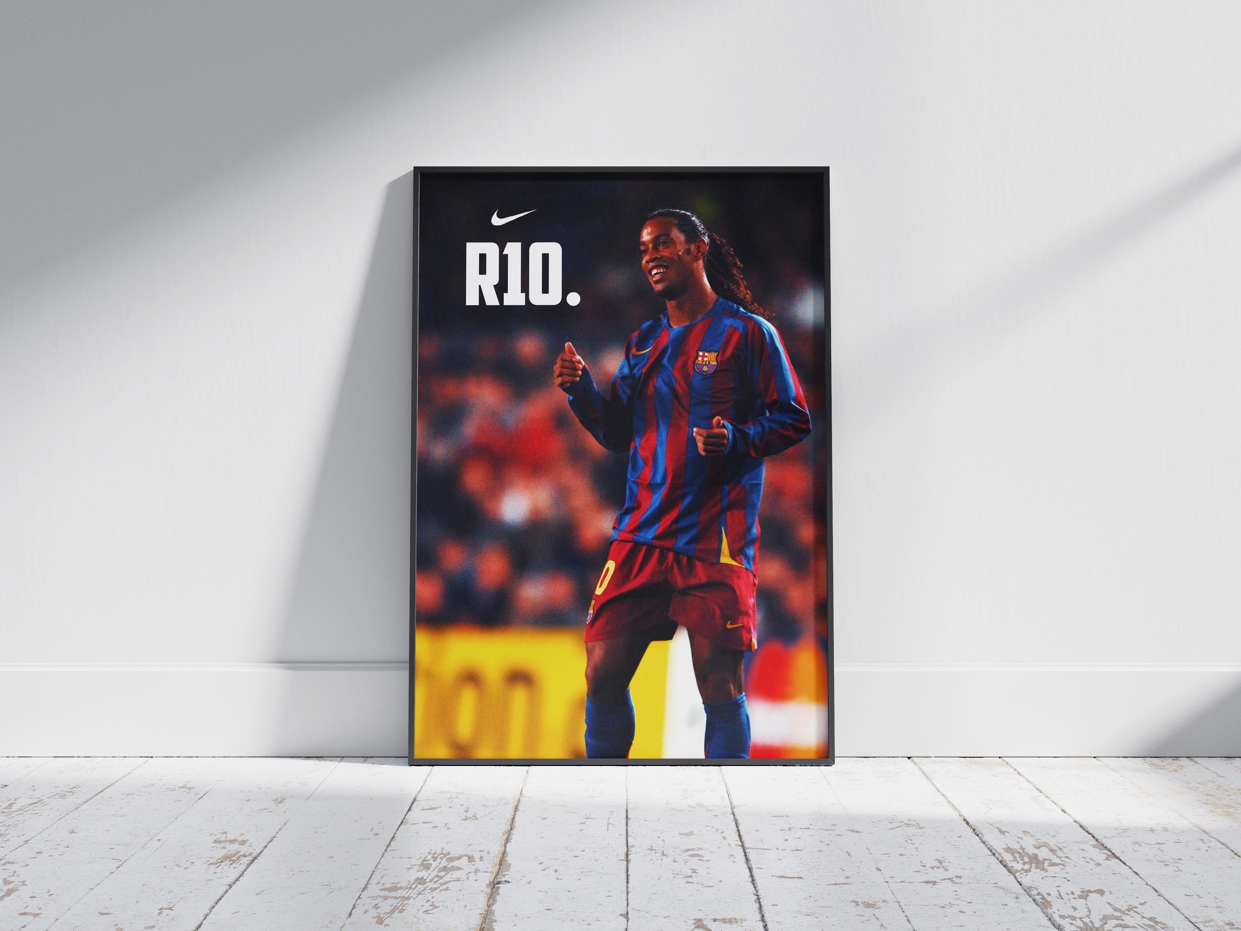 The Ronaldinho R10 Poster by Retro1999 shows the soccer legend in a red and blue striped jersey, smiling with thumbs up. Featuring the Nike logo and a UEFA Champions League tribute, it’s ideal for football fans. Framed and displayed on a wooden floor.