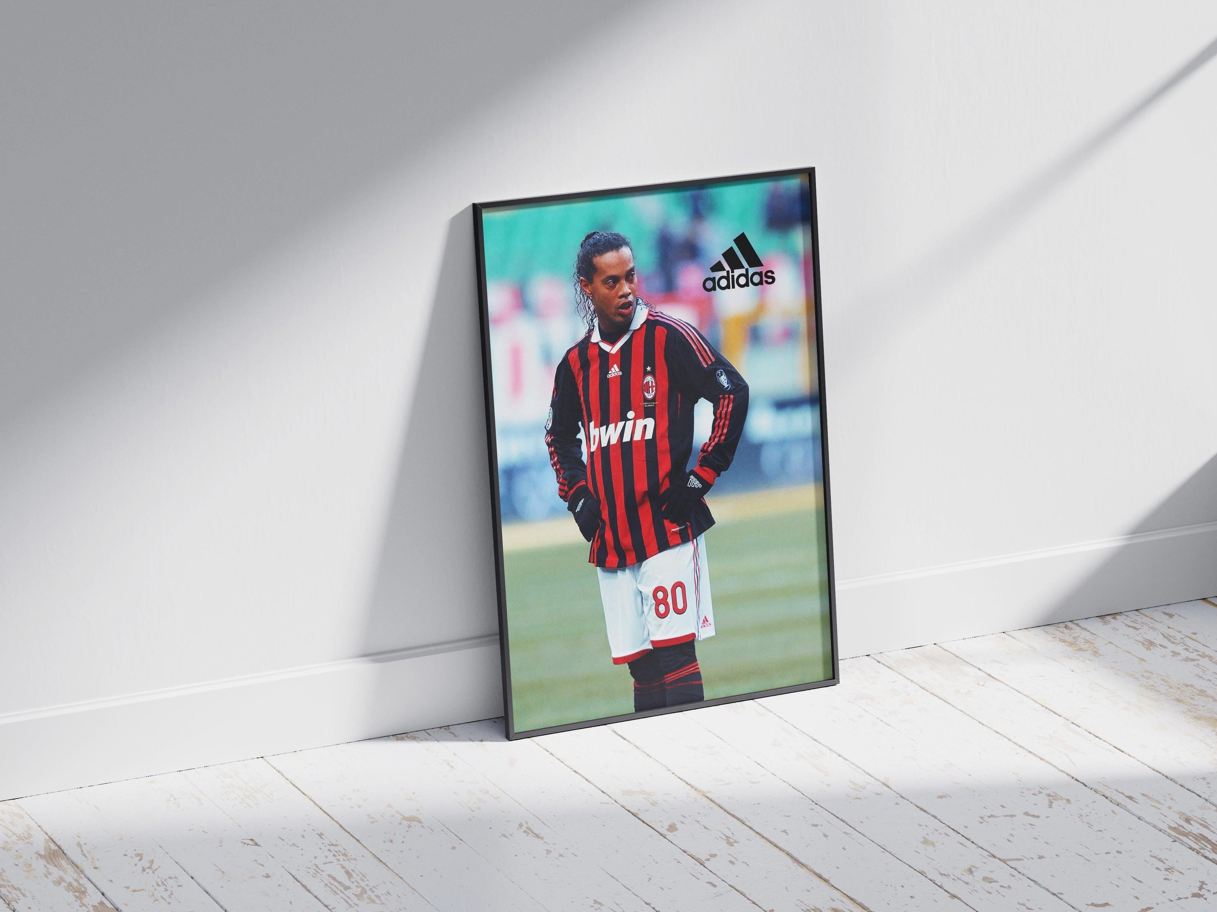 The Ronaldinho x AC Milan Poster by Retro1999 shows Ronaldinho in an AC Milan jersey with number 80 on the field, framed and leaning against a white wall on a wooden floor. The Adidas logo appears at the top right.