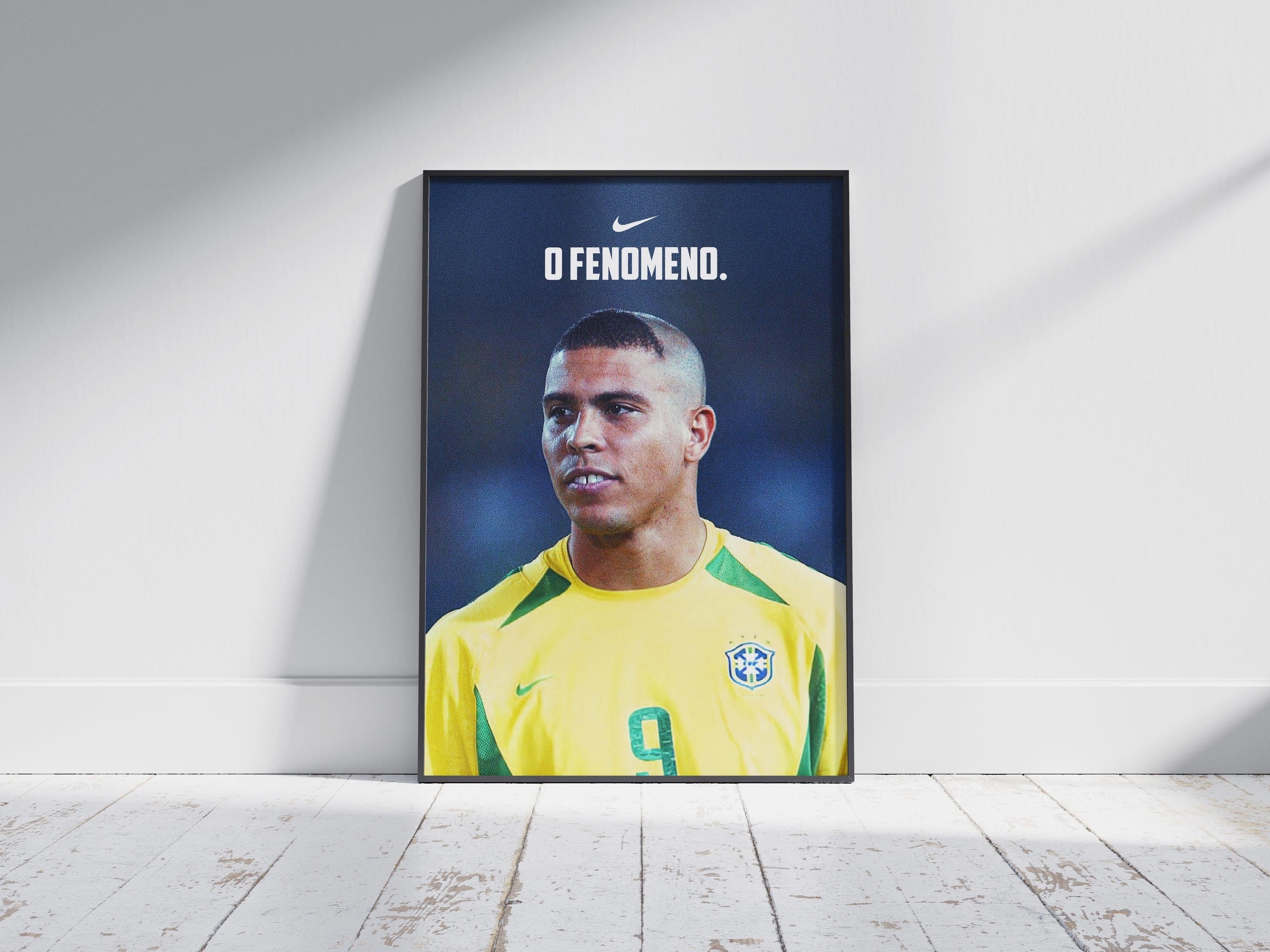 The Ronaldo O Fenômeno Poster by Retro1999 shows the football legend in a yellow jersey with green accents and number 9, celebrating his iconic FIFA World Cup 2002 victory, displayed framed on a wooden floor.