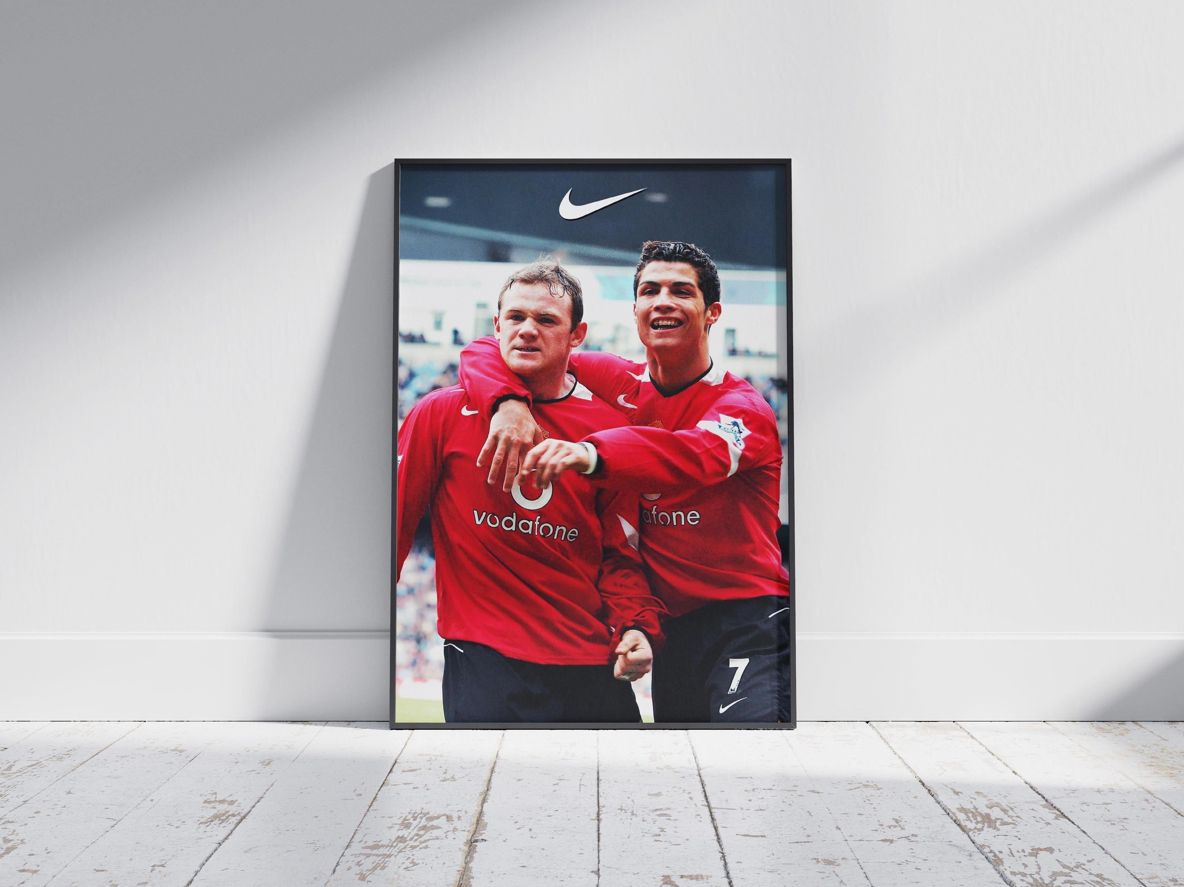 The Rooney x CR7 Poster by Retro1999 features two Manchester United legends in red jerseys celebrating on the pitch, with one’s arm around the other—an iconic football moment perfect for any fans collection.