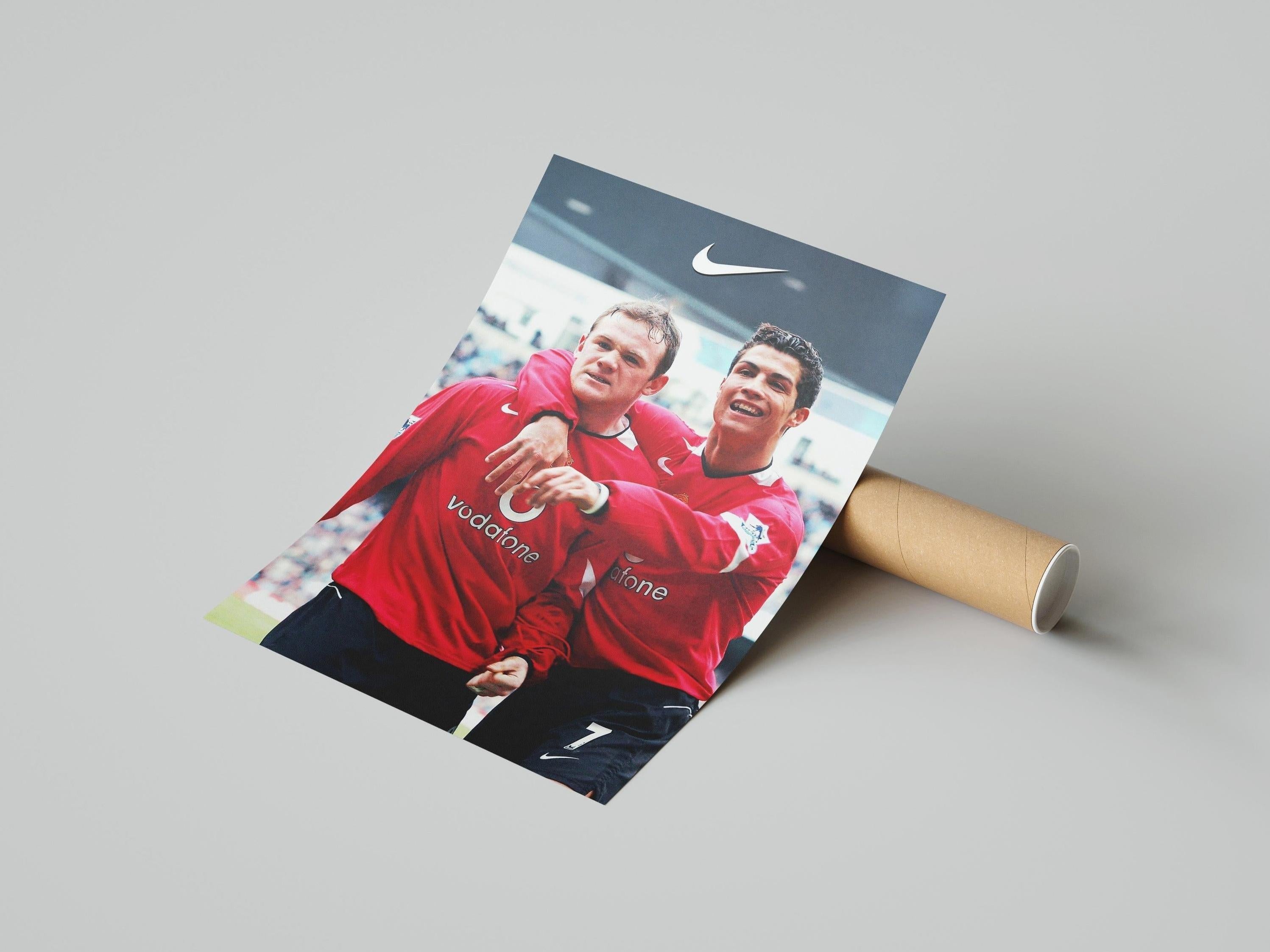 The Retro1999 Rooney x CR7 Poster shows two soccer players in red jerseys celebrating on the field, smiling and embracing, with iconic imagery and a Nike logo at the top. Poster comes rolled-up for easy handling.