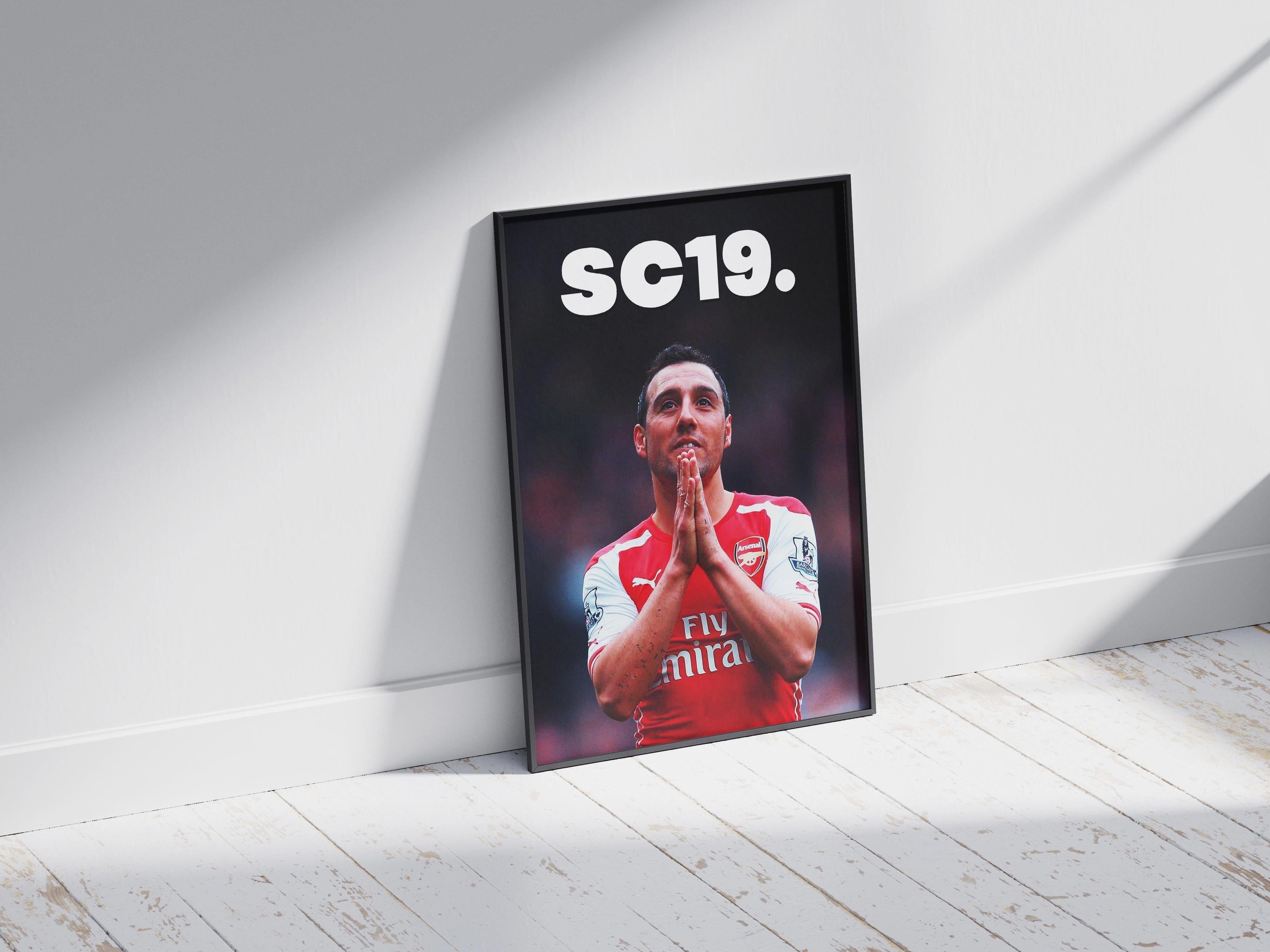 The Retro1999 Santi Cazorla SC19 Poster features the Arsenal star in his iconic kit, framed and set on a wooden floor with sunlight casting dramatic shadows on the surrounding white wall and floor.