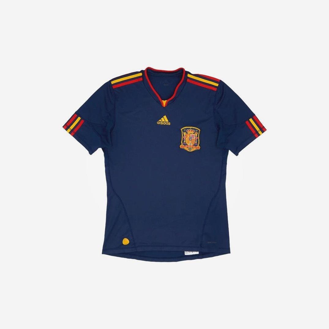 The Spain 2010 Away Shirt by Retro1999 is a navy blue jersey with red and yellow stripes, featuring the Spain crest and an authentic design inspired by the classic 2010 away kit.
