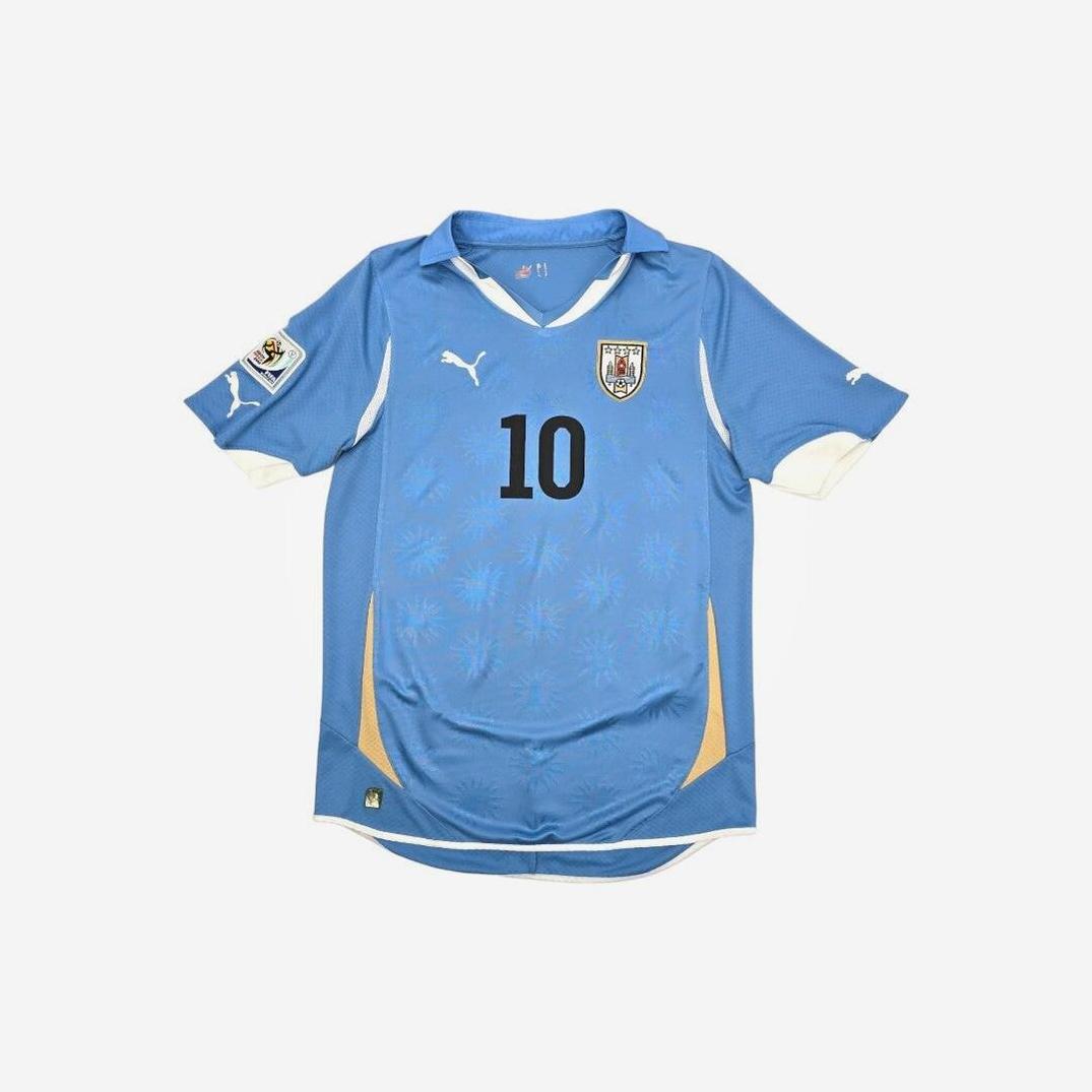 The Retro1999 Uruguay 2010 Home Shirt features authentic blue design with number 10, Puma logo, national crest, a tournament patch on the left sleeve, and retro-inspired gold and white accents.