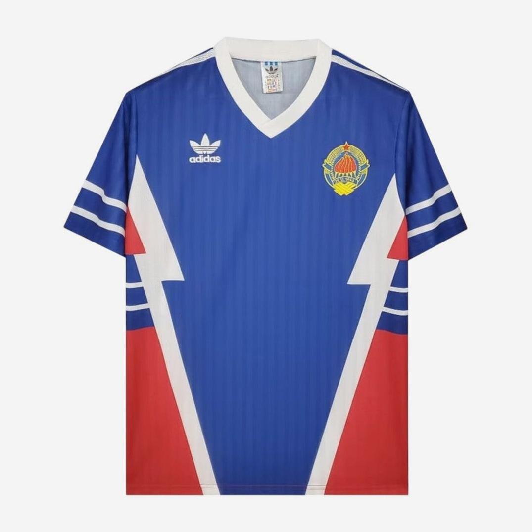 The Retro1999 Yugoslavia 1990 Home Shirt is a blue soccer jersey with a white V-neck, white and red geometric patterns, a left chest crest, and right logo—ideal for vintage sportswear fans.