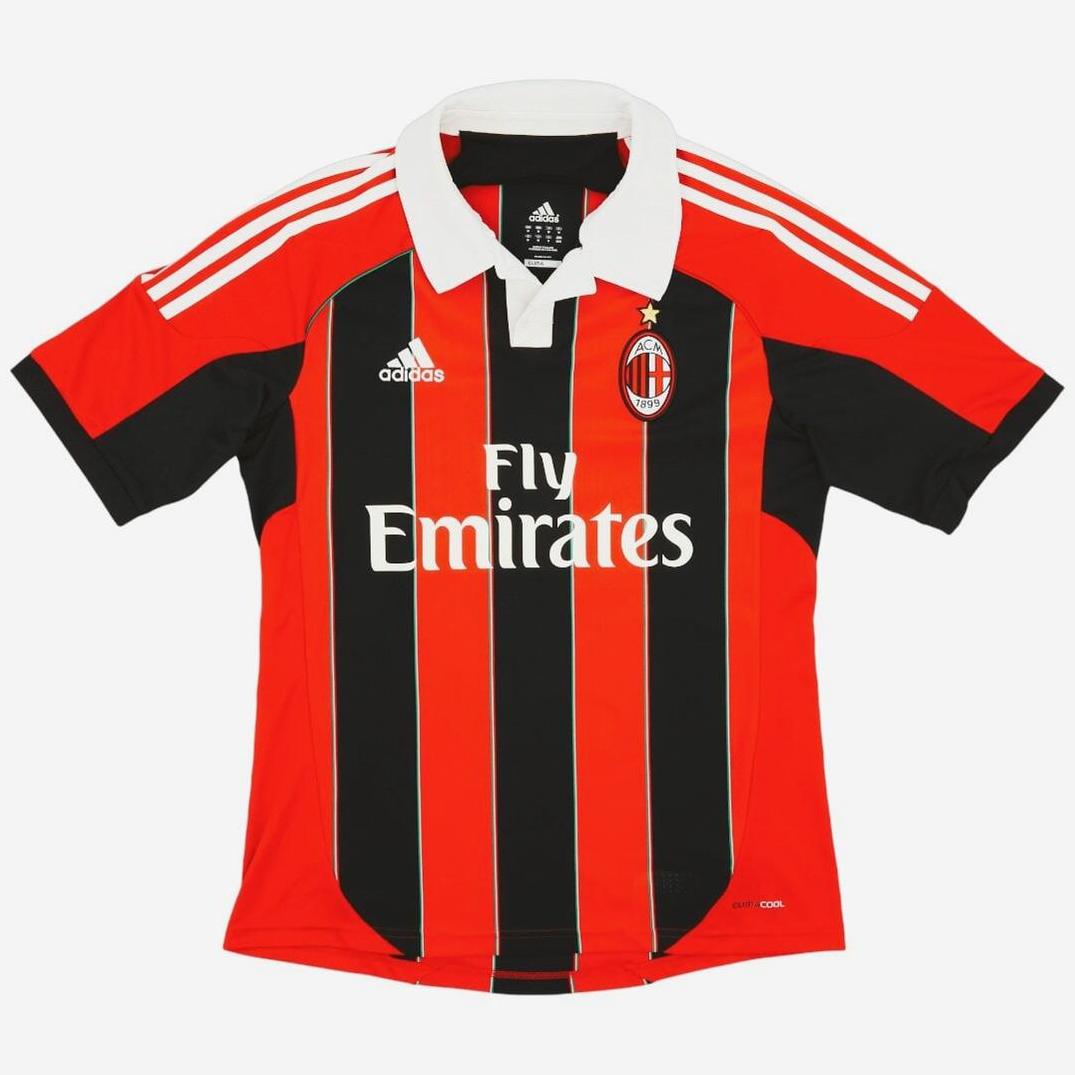 The AC Milan 2012-13 Home Shirt by Retro1999 features red and black stripes, white collar, Adidas logo, club crest, Fly Emirates sponsor on the front, and white shoulder stripes—a must-have for fans and collectors.