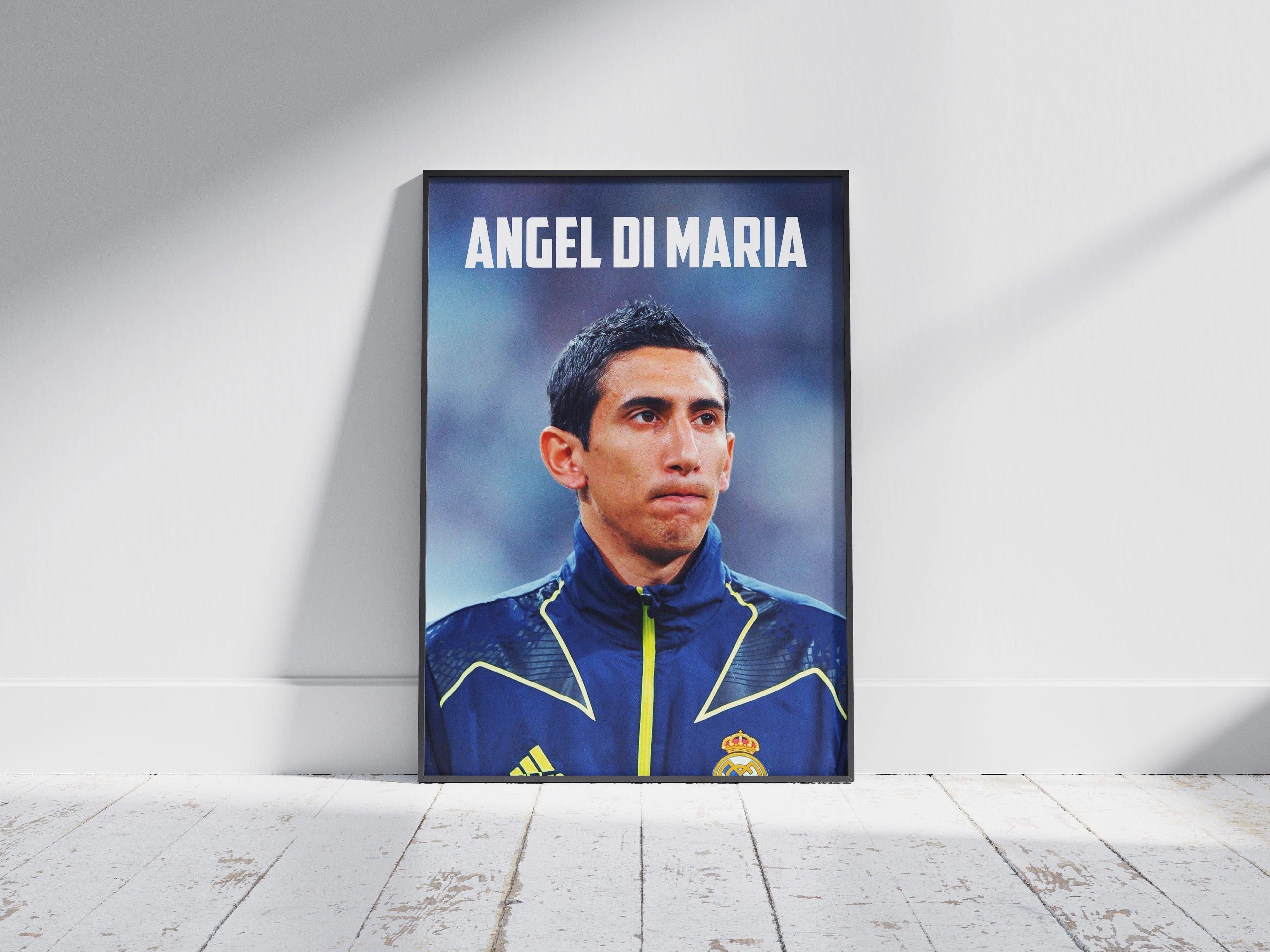 The Retro1999 Angel Di Maria RMA Poster features the soccer star in a blue jacket with yellow accents, labeled ANGEL DI MARIA, framed and displayed against a white wall on a wooden floor—a perfect tribute for football fans.