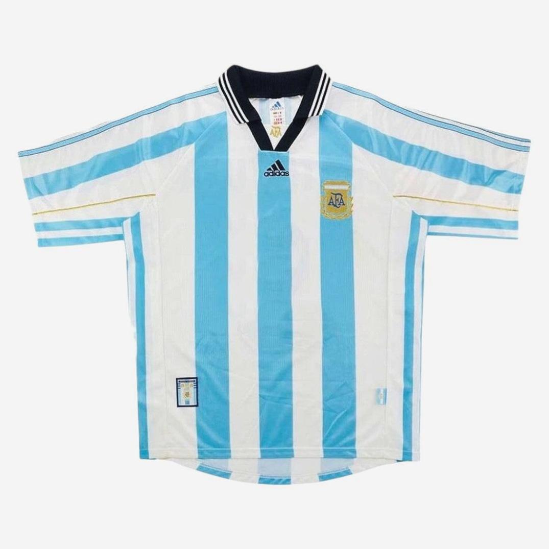 The Retro1999 Argentina 1998 Home Shirt features iconic light blue and white stripes, a black collar with white trim, and the team crest—an authentic retro kit inspired by Argentine football history.