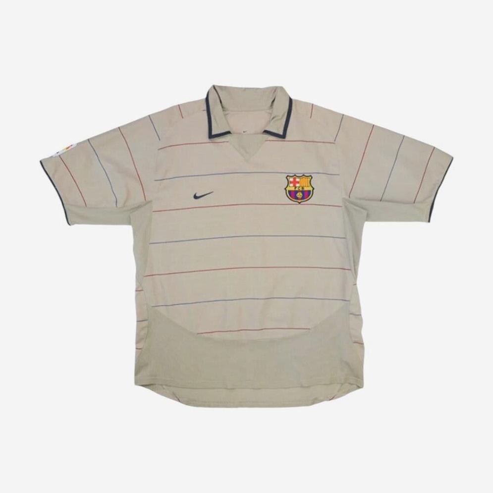 The Barcelona 2003-04 Away Shirt by Retro1999 features a beige base, thin red and blue stripes, Nike chest logo, and club crest—ideal for fans after a nostalgic or retro football kit.
