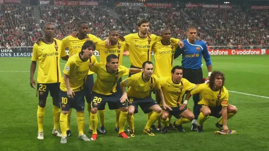 A soccer team wearing Retro1999 Barcelona 2008-09 Away Shirts poses for a group photo on the field, with a packed stadium in the background.