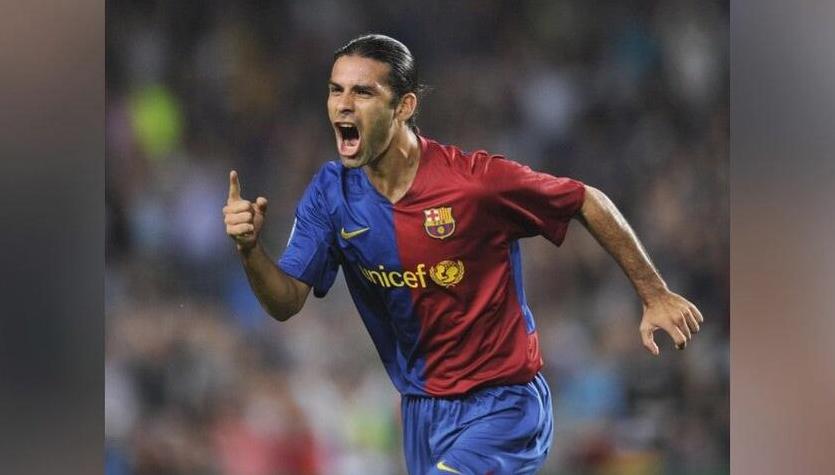 A soccer player celebrates passionately on the field in the Retro1999 Barcelona 2008-09 Home Shirt, mouth open and finger pointed upward, with a blurred crowd in the background—an iconic football moment.