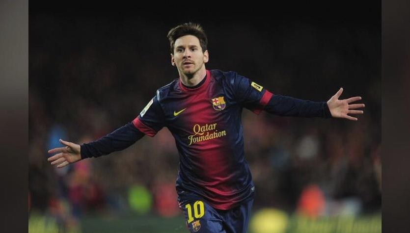 A soccer player wearing the Retro1999 Barcelona 2012-13 Home Shirt with number 10 celebrates with outstretched arms on the field after a La Liga win, the background blurred with fans in the stands.