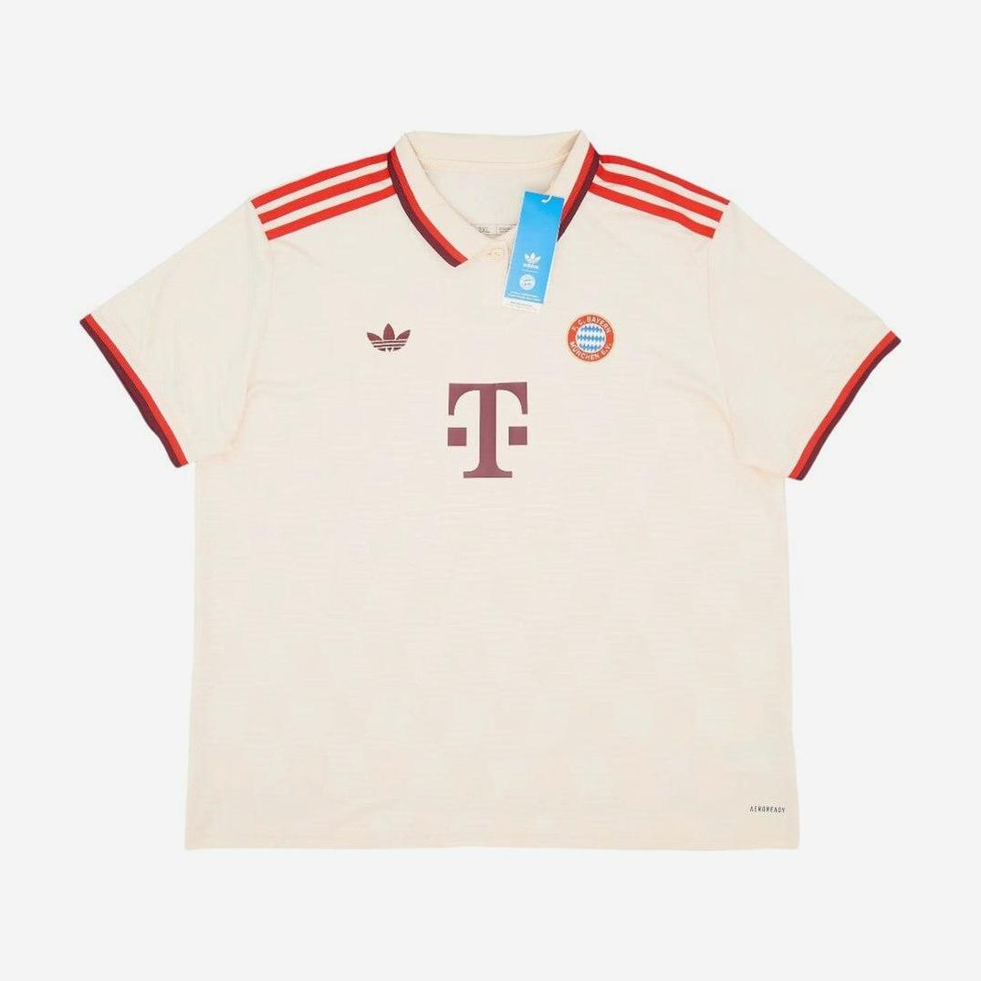 The Retro1999 Bayern Munich 2024-25 Third Shirt is cream-colored with red accents, Adidas stripes on the shoulders, club and Adidas logos on the chest, and a Telekom sponsor logo in the center. A blue tag from the collar adds a retro touch.