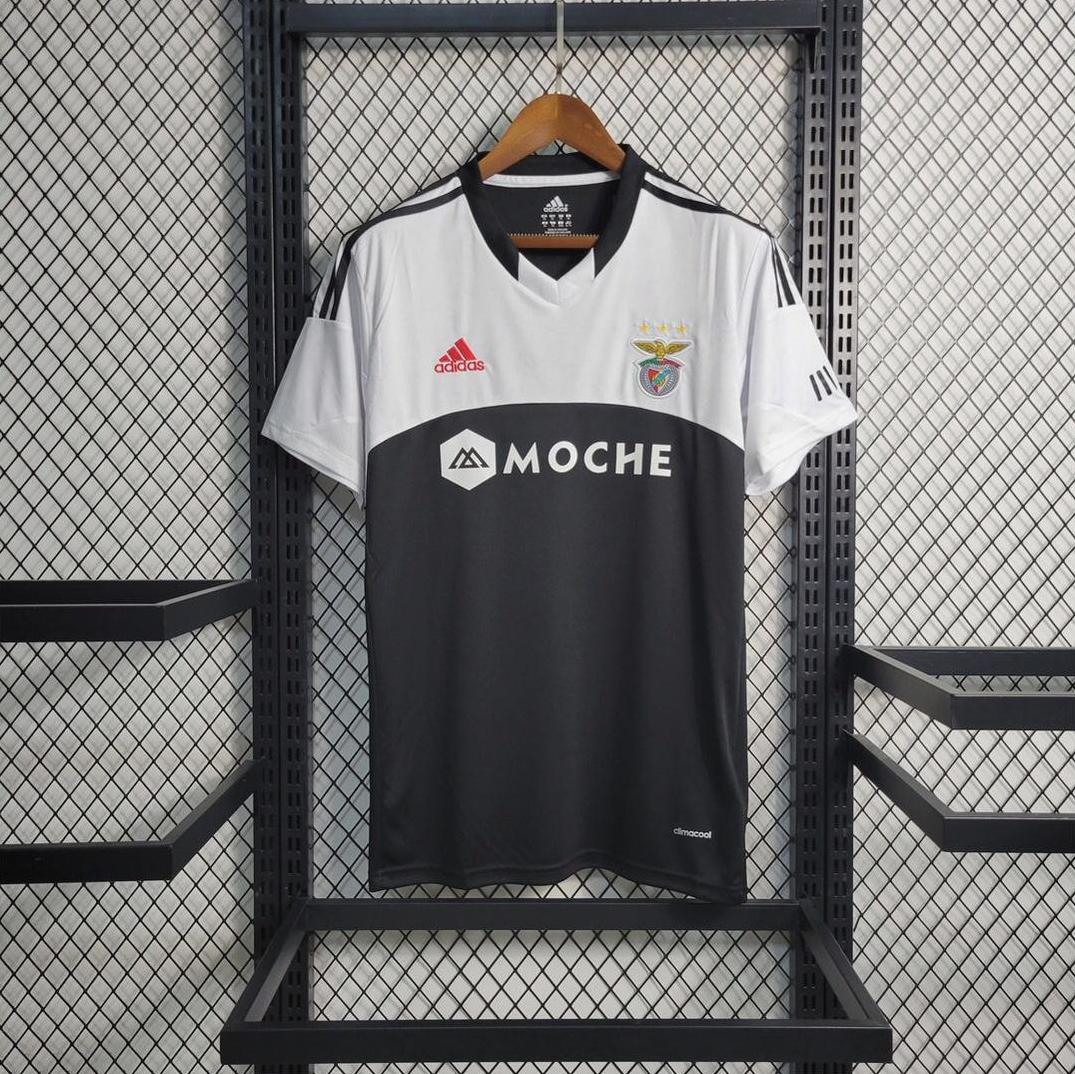 A Retro1999 Benfica 2013-14 Away Shirt with the Moche sponsor logo hangs on a wooden hanger against a metal mesh wall, highlighting this classic black and white football club merchandise.