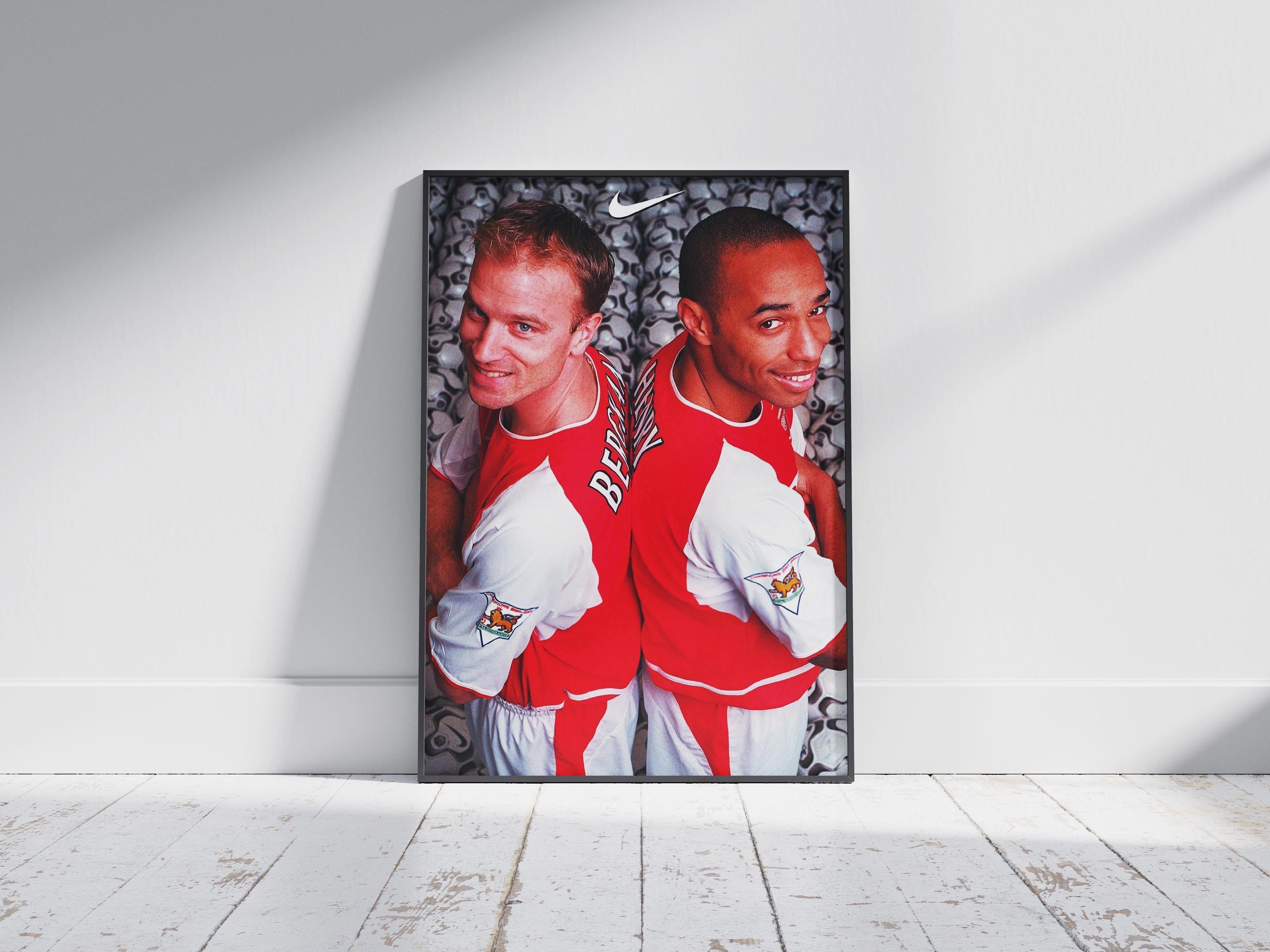 The Bergkamp x Henry Poster by Retro1999 features two Arsenal legends in red and white jerseys, standing back to back on a background of soccer balls—ideal sports decor or a football memorabilia collectible.