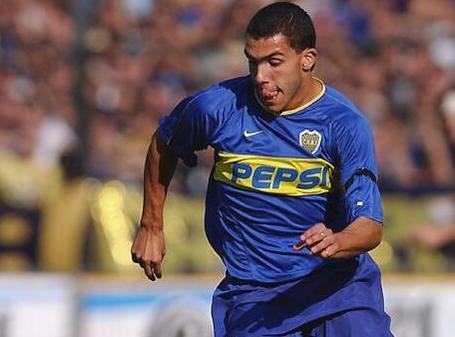 A soccer player wearing the Retro1999 Boca Juniors 2003-04 Home Shirt with a Pepsi logo runs on the field during a match, as blurred spectators watch in the background.