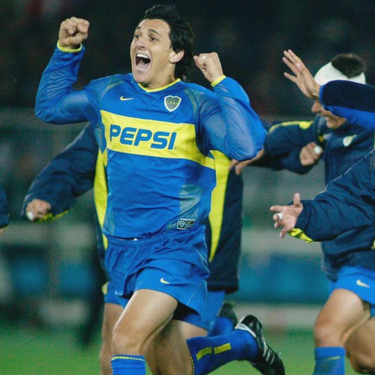 A soccer player celebrates in the Retro1999 Boca Juniors 2003-04 Home Shirt, blue and yellow with a PEPSI logo, echoing the excitement of the 2004 Copa Sudamericana era as teammates gather on the field.