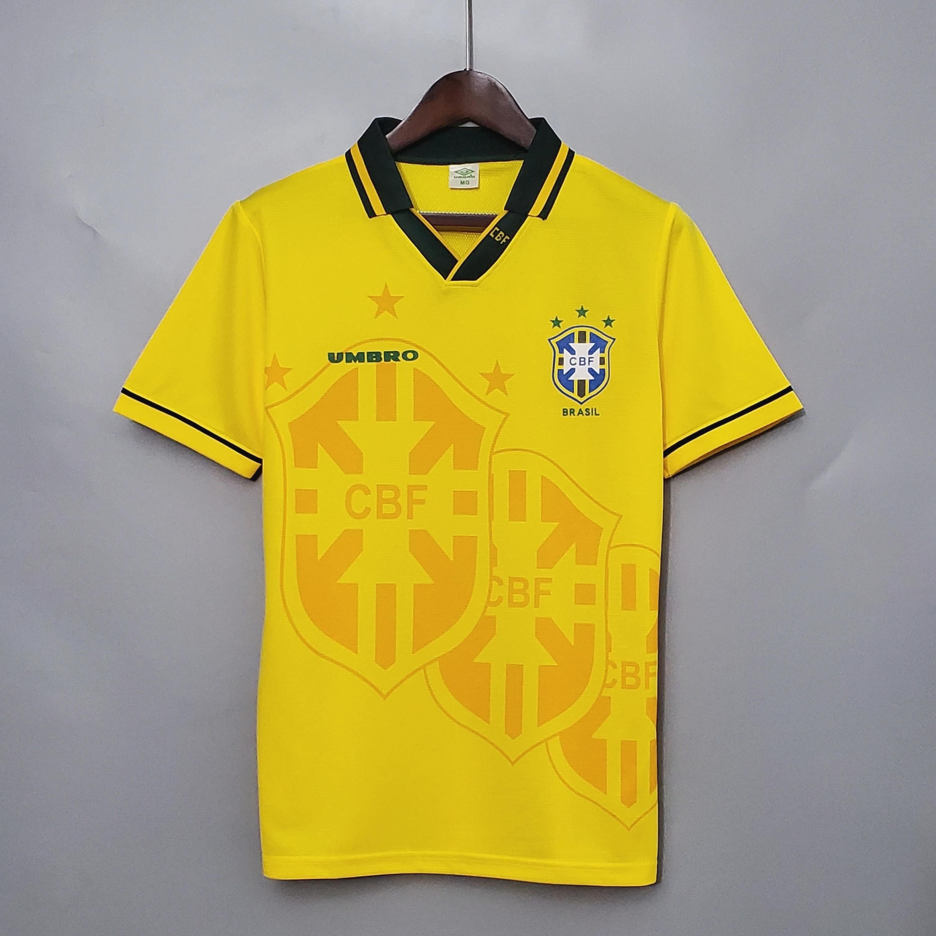 A yellow Brazil 1993-94 Home Shirt by Retro1999 hangs on a wooden hanger, featuring green accents, the CBF crest with five stars, and a large faded CBF logo pattern—a true piece of Brazilian football history.