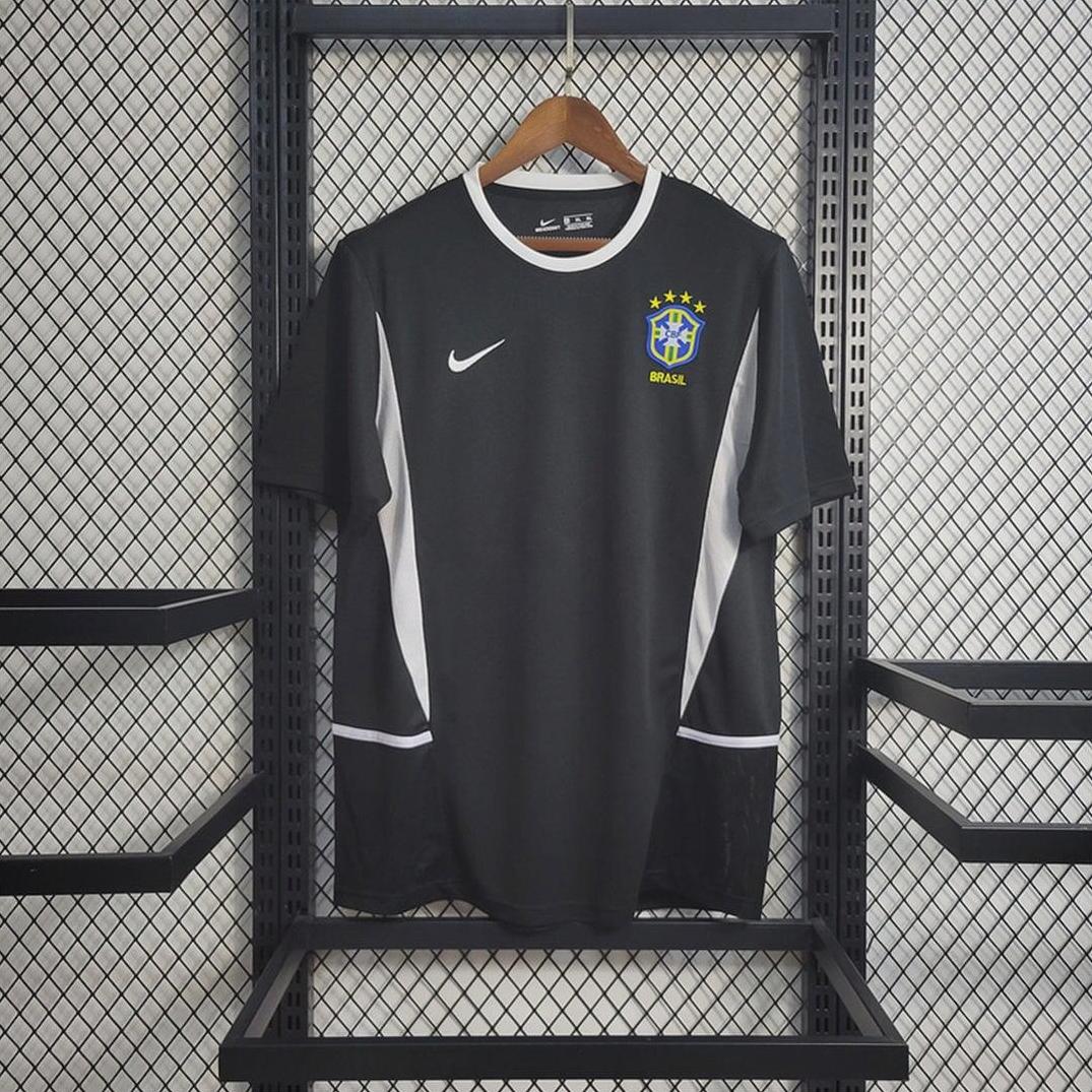 A Brazil 2002 Black Goalkeeper Shirt by Retro1999 with white details hangs on a wooden hanger against a black wire mesh, featuring an authentic design inspired by the classic retro kit.