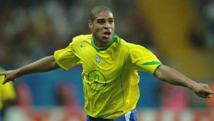A soccer player celebrates with arms outstretched on the field, wearing a Retro1999 Brazil 2004 Home Shirt. The blurred stadium background highlights the excitement of Brazilian football and the iconic design.